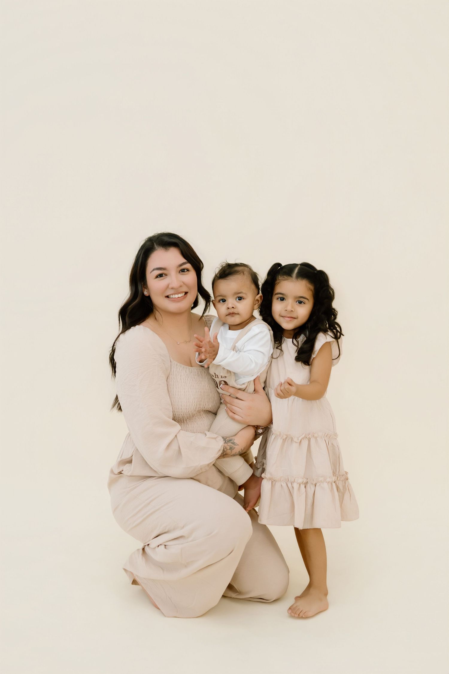 A family poses together in neutral beige outfits against a light background for a minimalist portrait session.