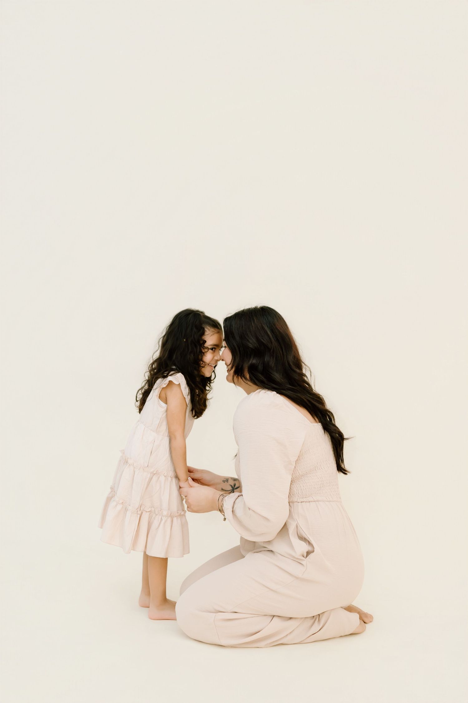 Mother and daughter in matching light pink outfits share tender moments in minimalist studio portraits.