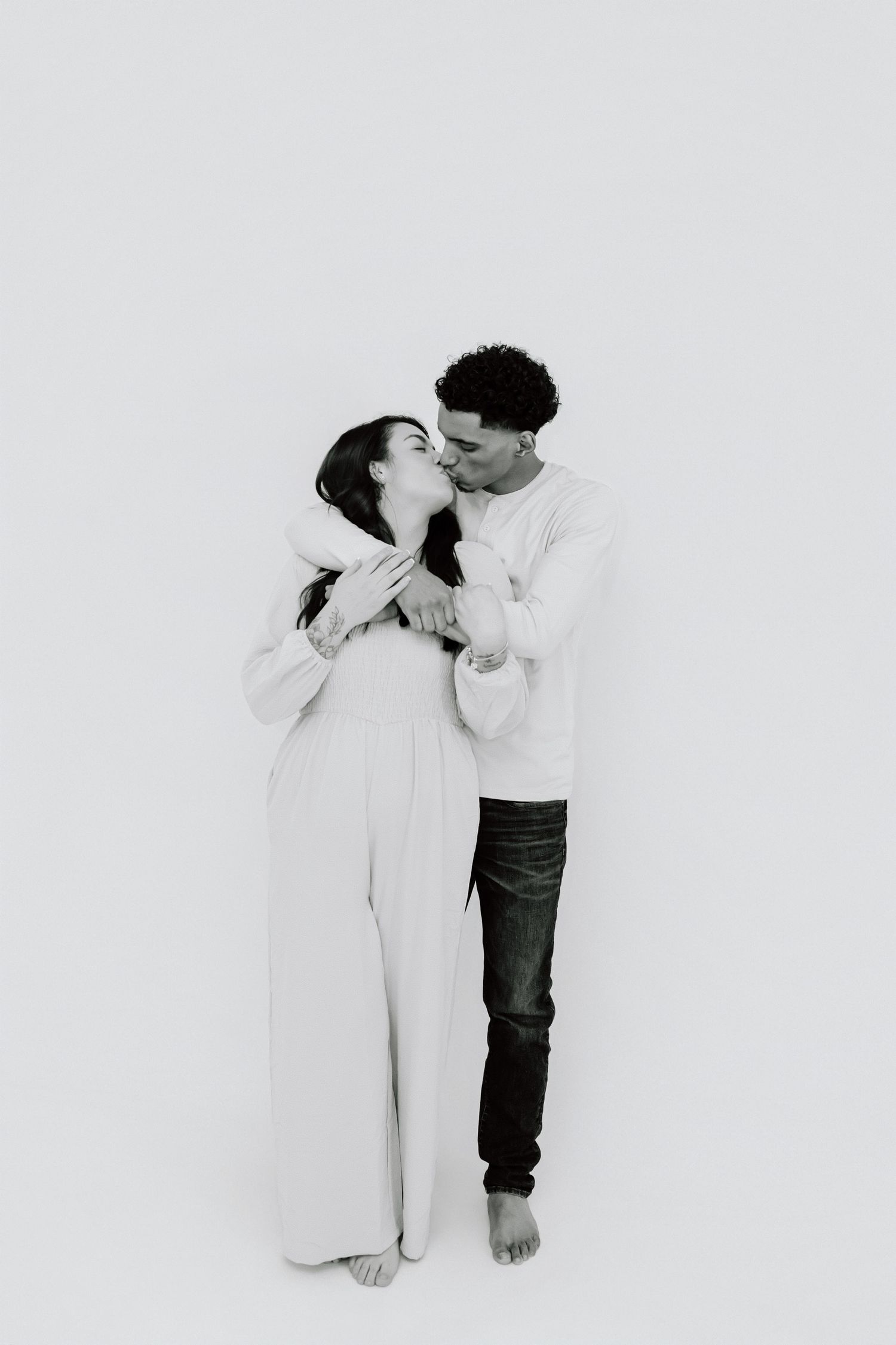 Two people in contrasting outfits embrace against a white background in a series of artistic black and white photos.
