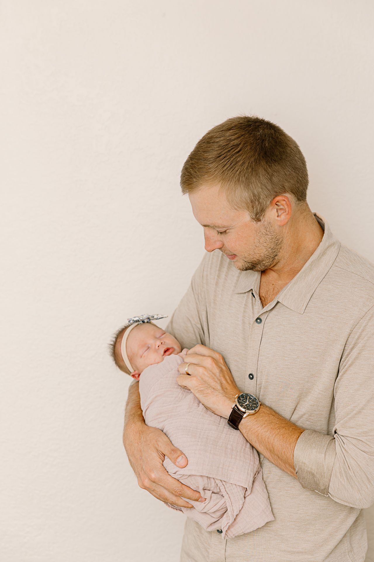 Adult in beige shirt tenderly holding sleeping newborn wrapped in light fabric.