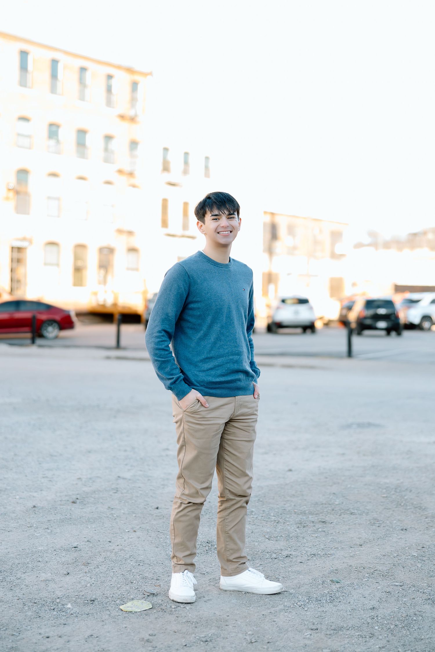 Full length portrait of person in blue sweater and khakis standing in urban parking area.