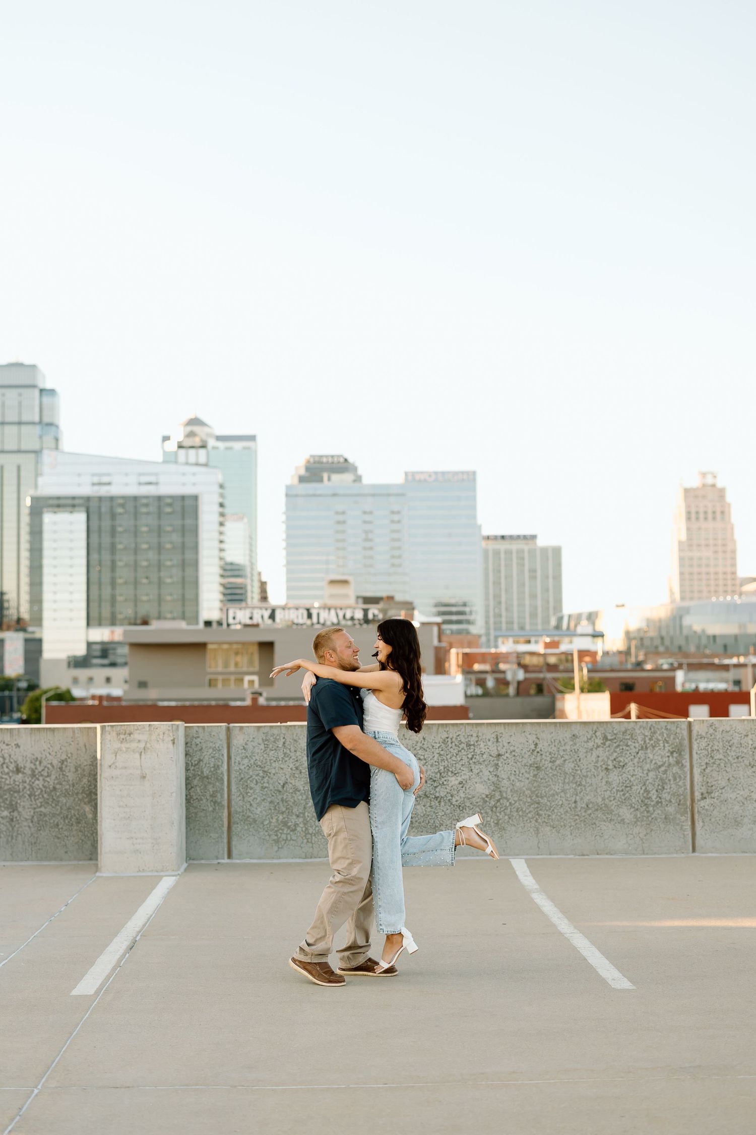 A romantic couple dances together on an urban rooftop with a city skyline visible in the background.