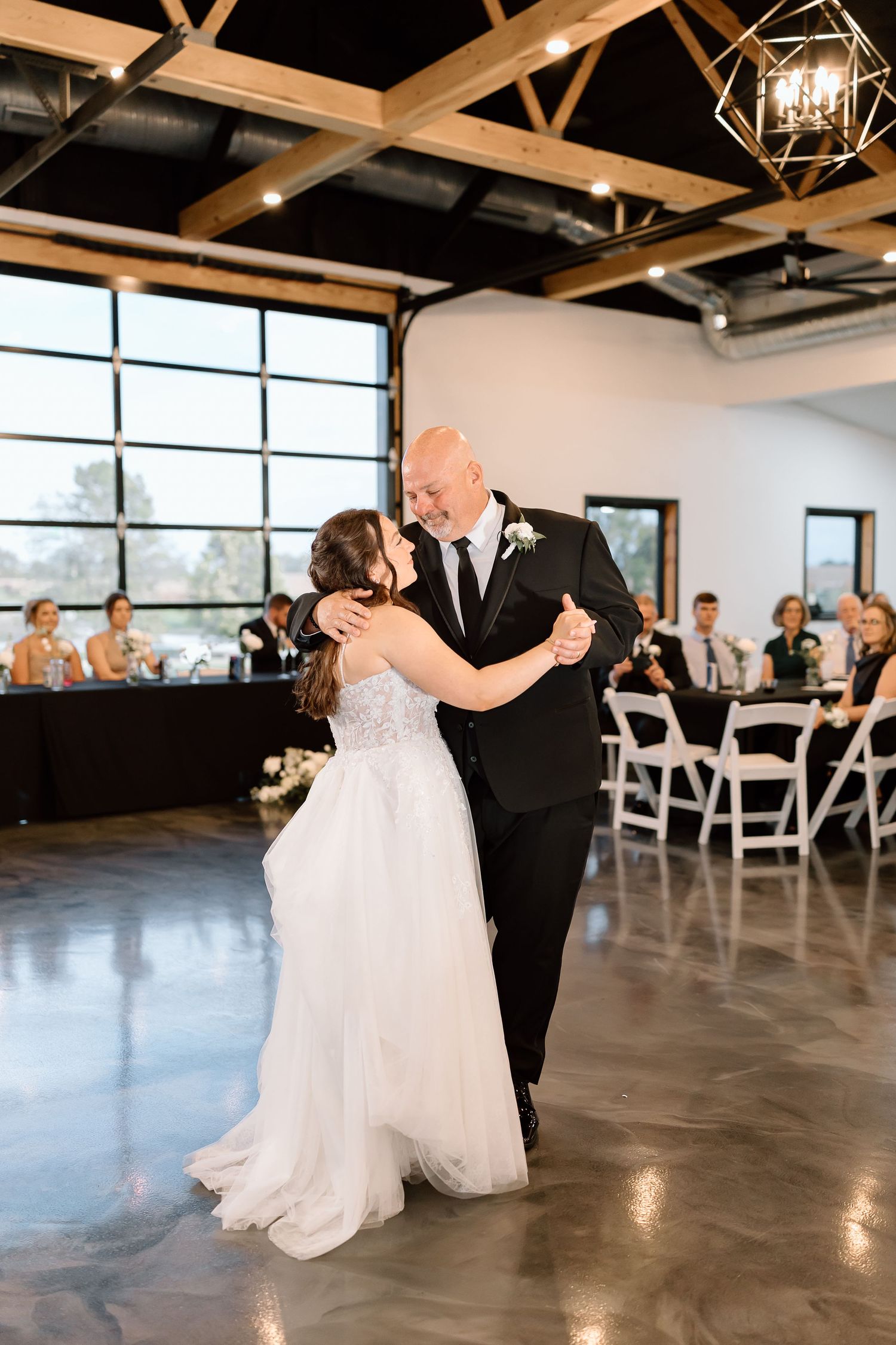 Couple sharing their first dance at a modern industrial wedding venue with exposed beams and large windows.