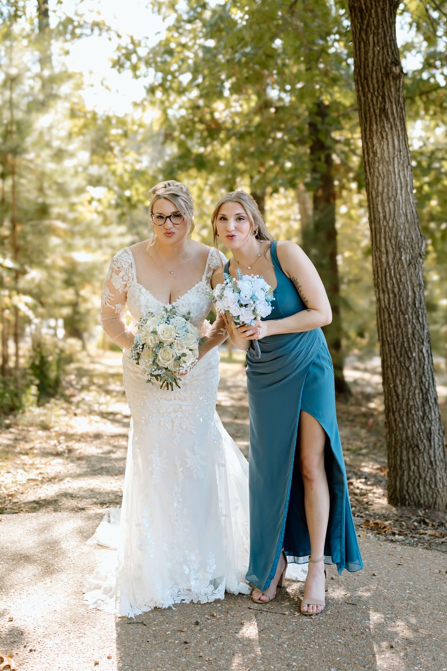 Wedding party members in teal dresses and white gown pose together in a sunlit forest setting.