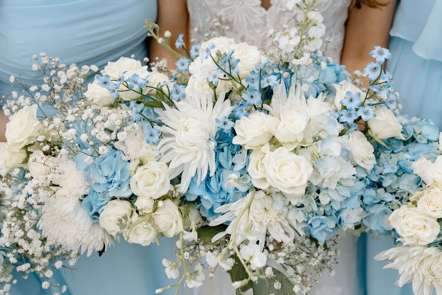 Blue and white wedding bouquets featuring roses, hydrangeas, and baby's breath held by bridesmaids in light blue dresses.