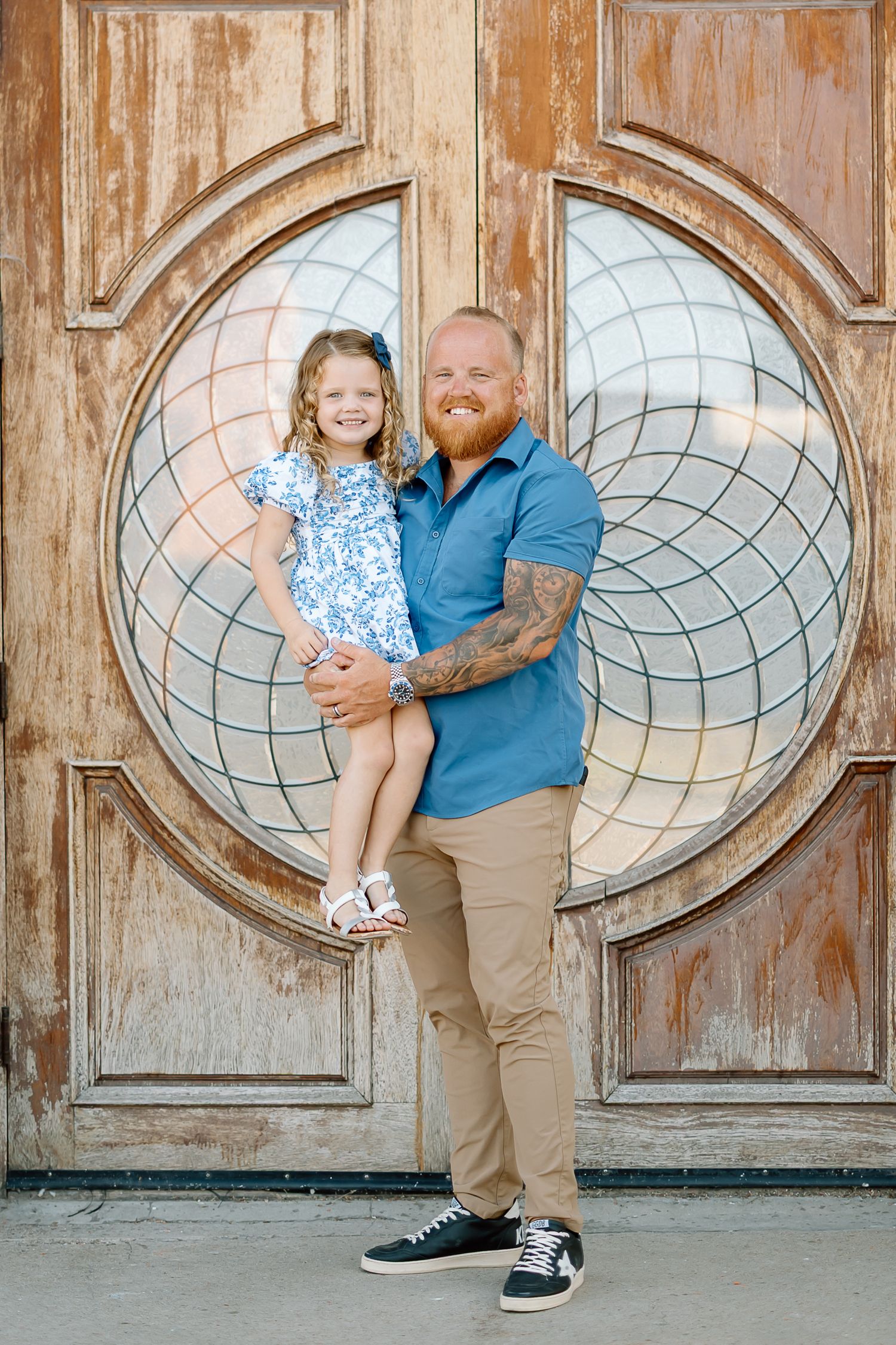 A parent and child pose together in front of a vintage wooden door with circular geometric design details.