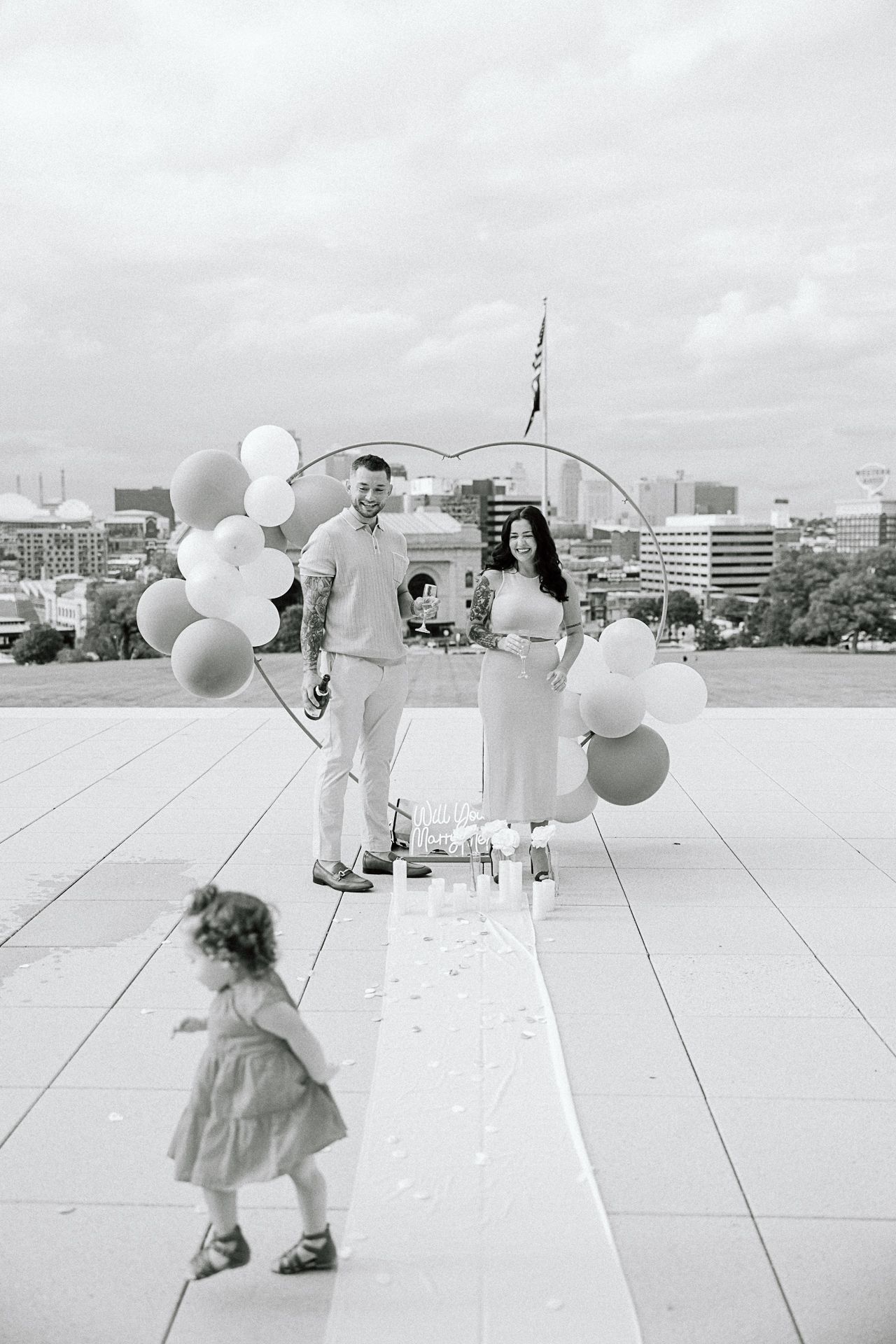 Black and white sequence of someone playing with white balloons on a rooftop against an urban skyline.