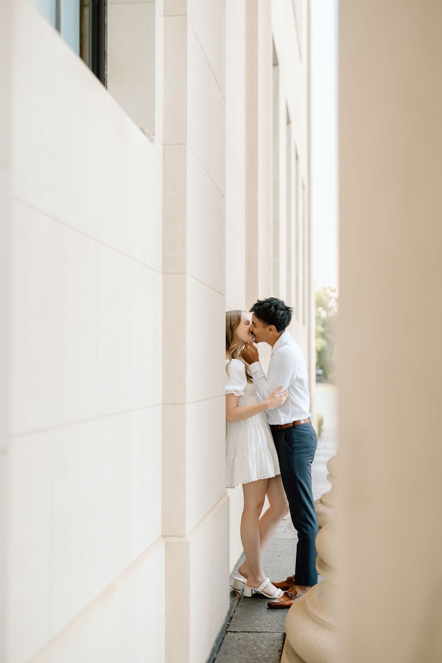 Romantic couple embraces in a minimalist white hallway with columns creating an elegant architectural backdrop.