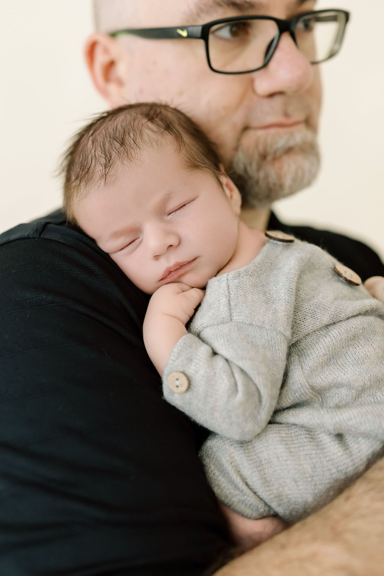 A baby wearing a gray sweater sleeps peacefully while being held in someone's arms.