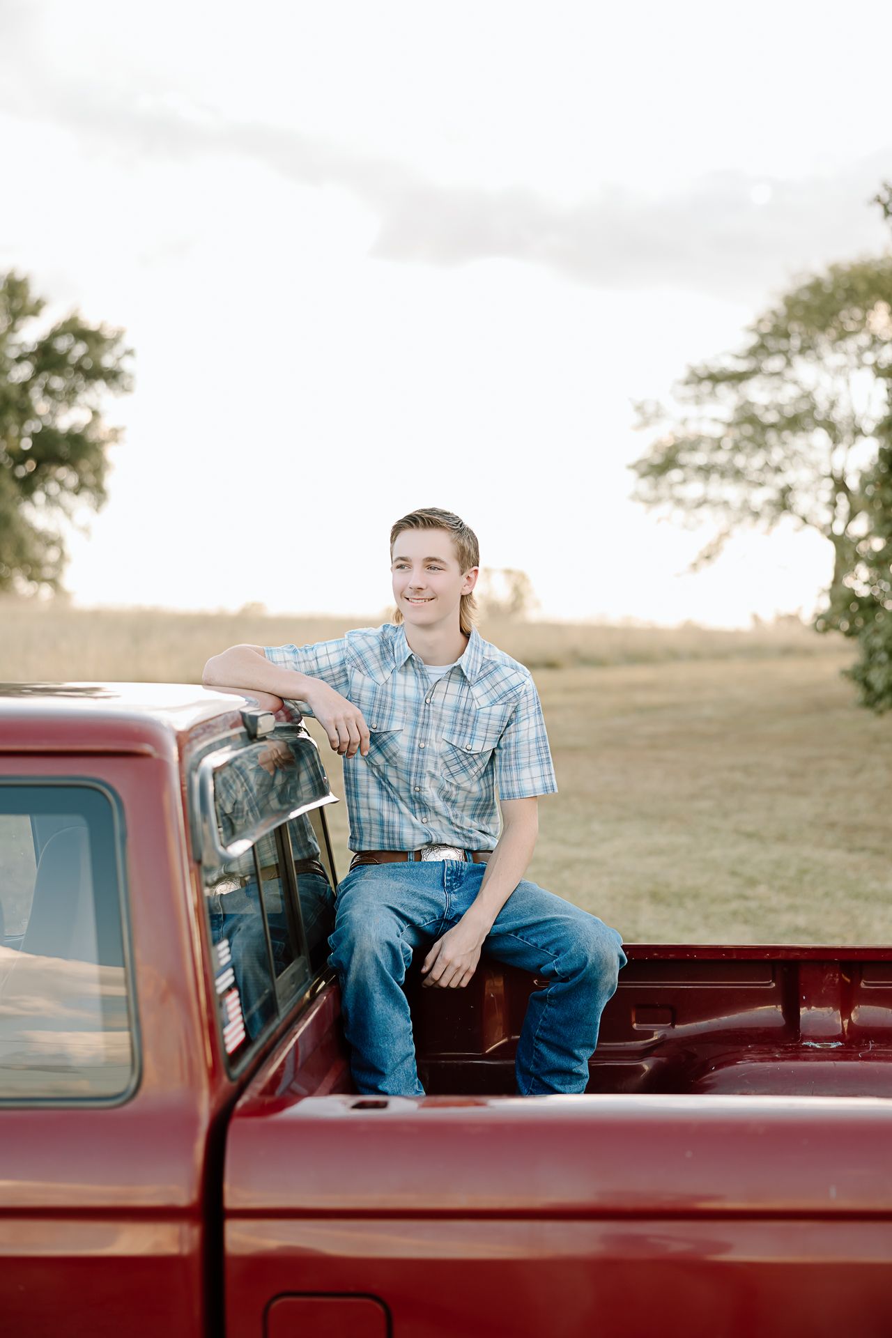 A vintage red pickup truck parked in a grassy field during golden hour.
