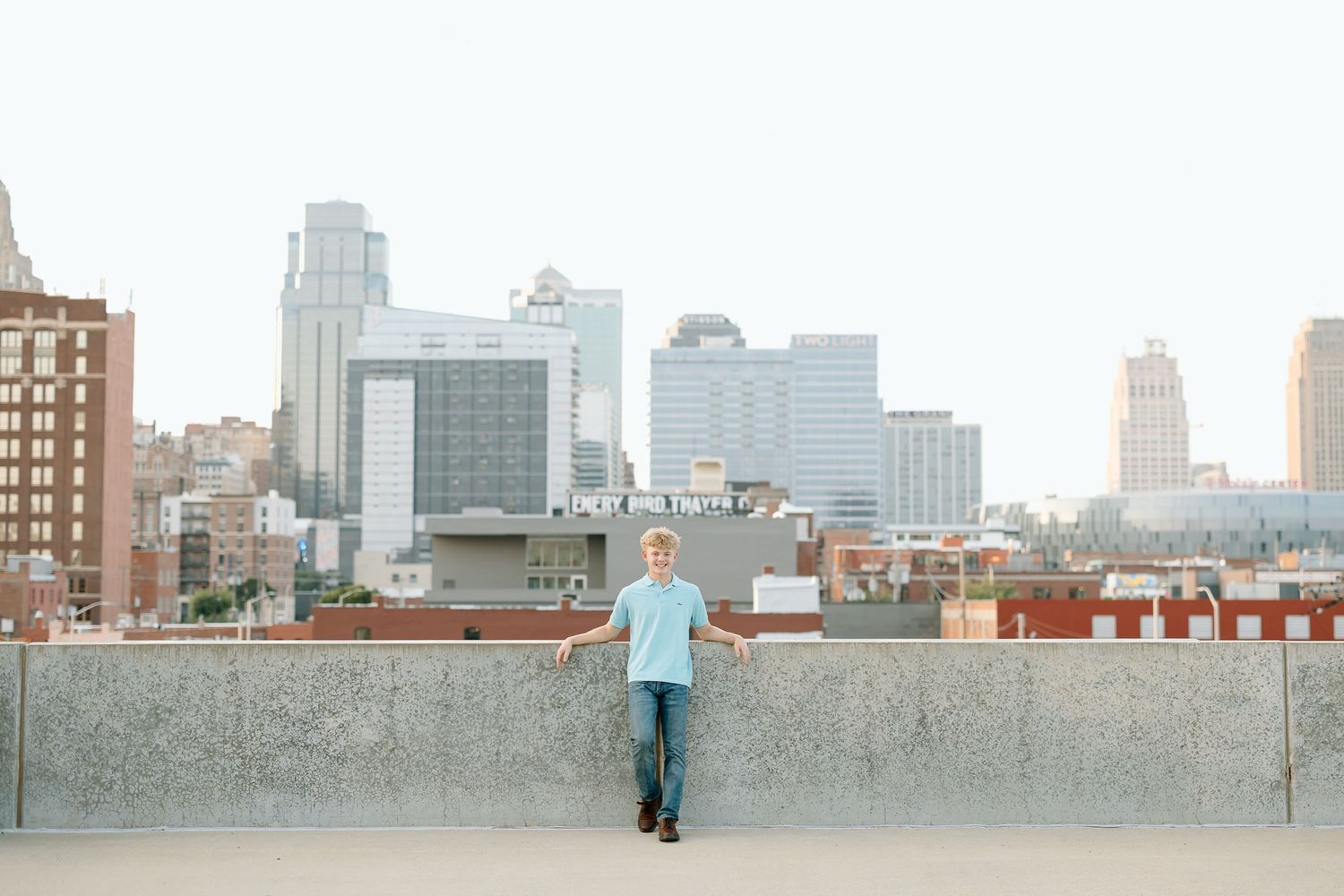 Person in light blue shirt stands on rooftop with Kansas City skyline in background during daytime.