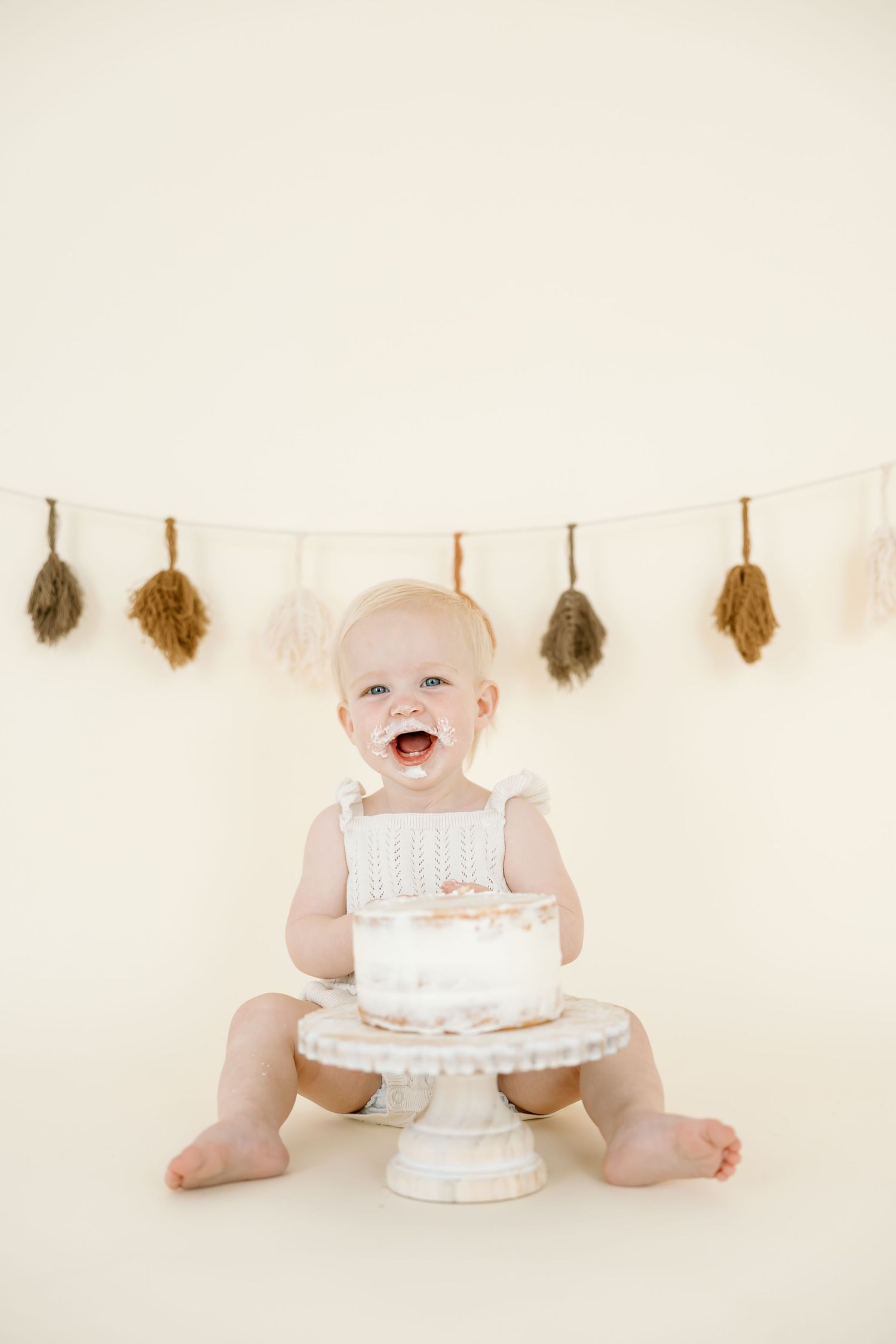 A series of four photos showing a baby in white clothing sitting with a birthday cake on a light beige background.