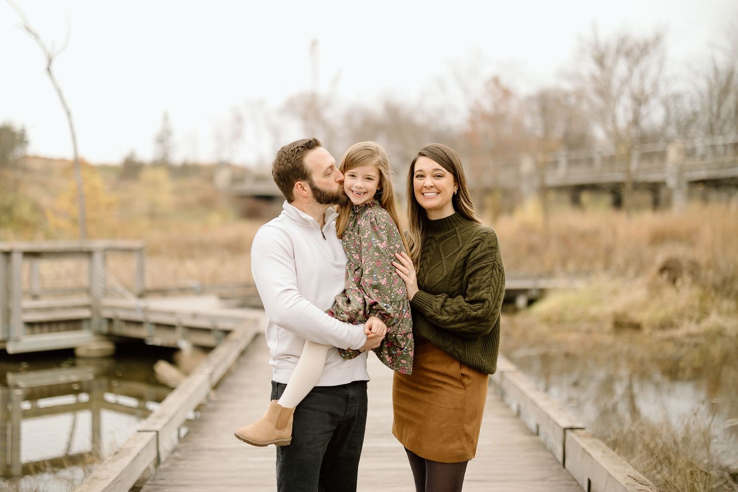 A loving family shares tender moments while standing on a wooden boardwalk in autumn.