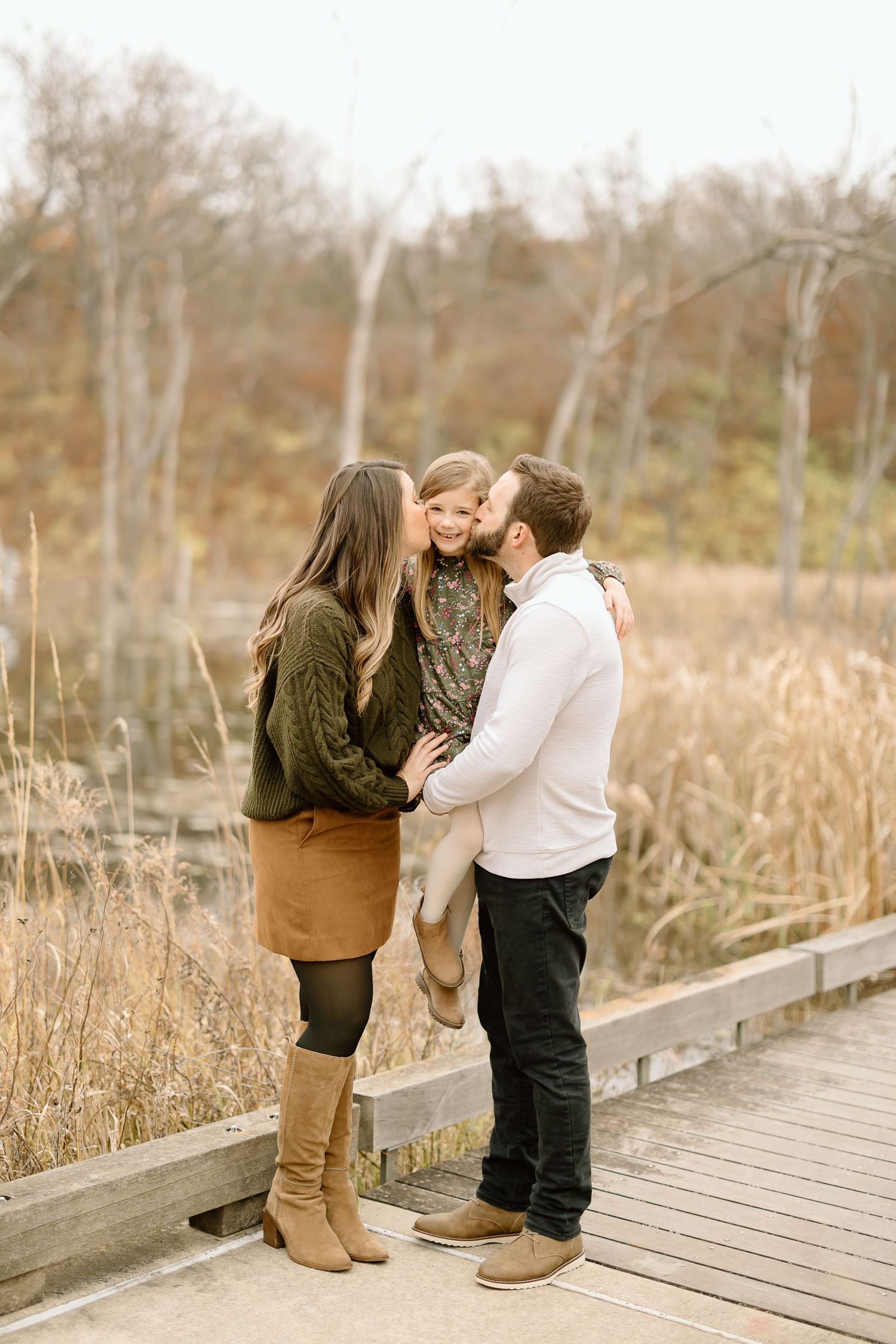 Family sharing tender moment on wooden boardwalk surrounded by autumn scenery.