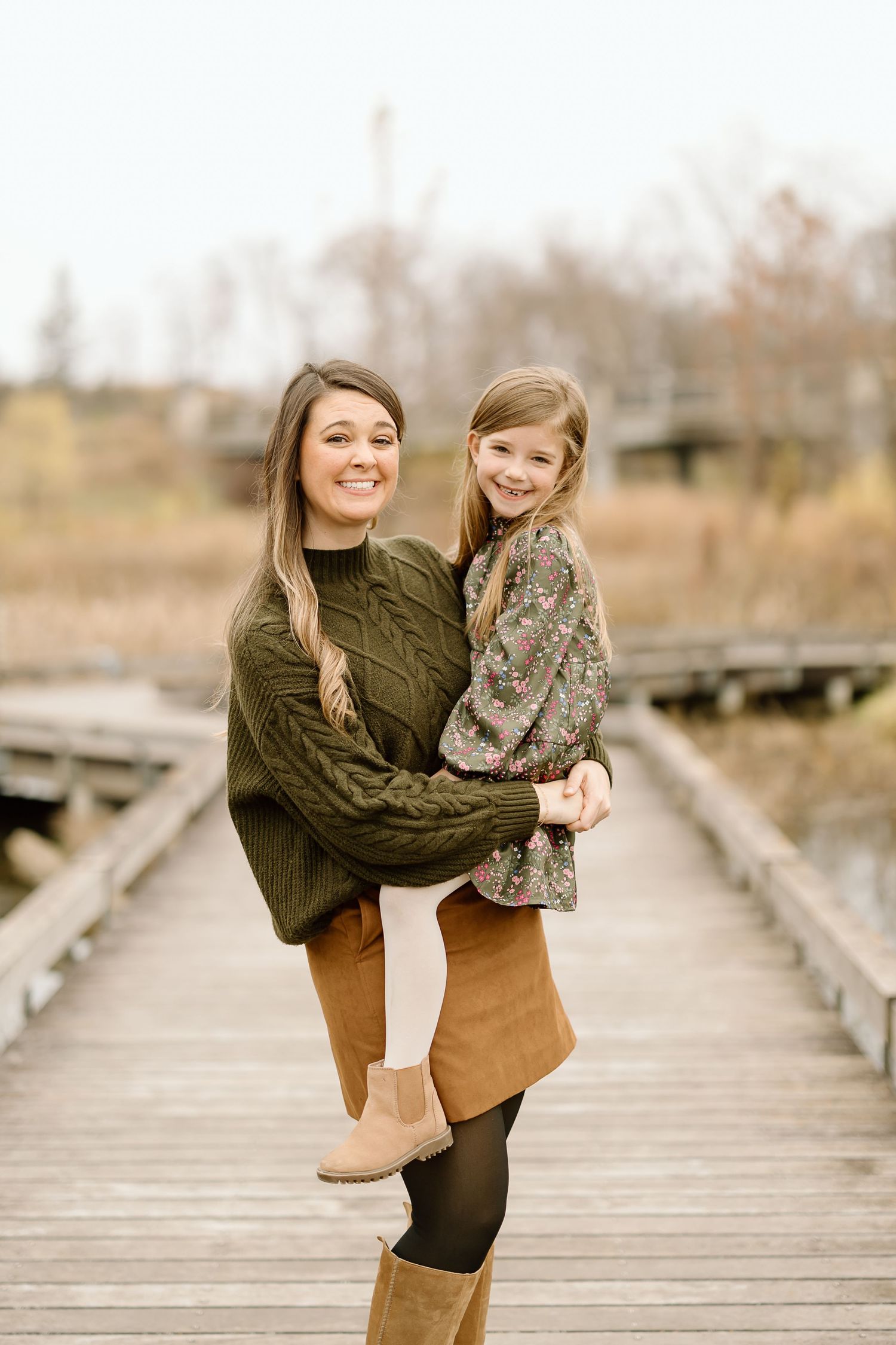 A tender moment captured on a wooden boardwalk in autumn with olive sweater and brown skirt styling.