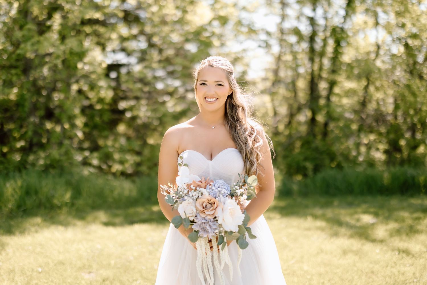 Bride holding soft pink and white bouquet in sunlit outdoor garden setting.