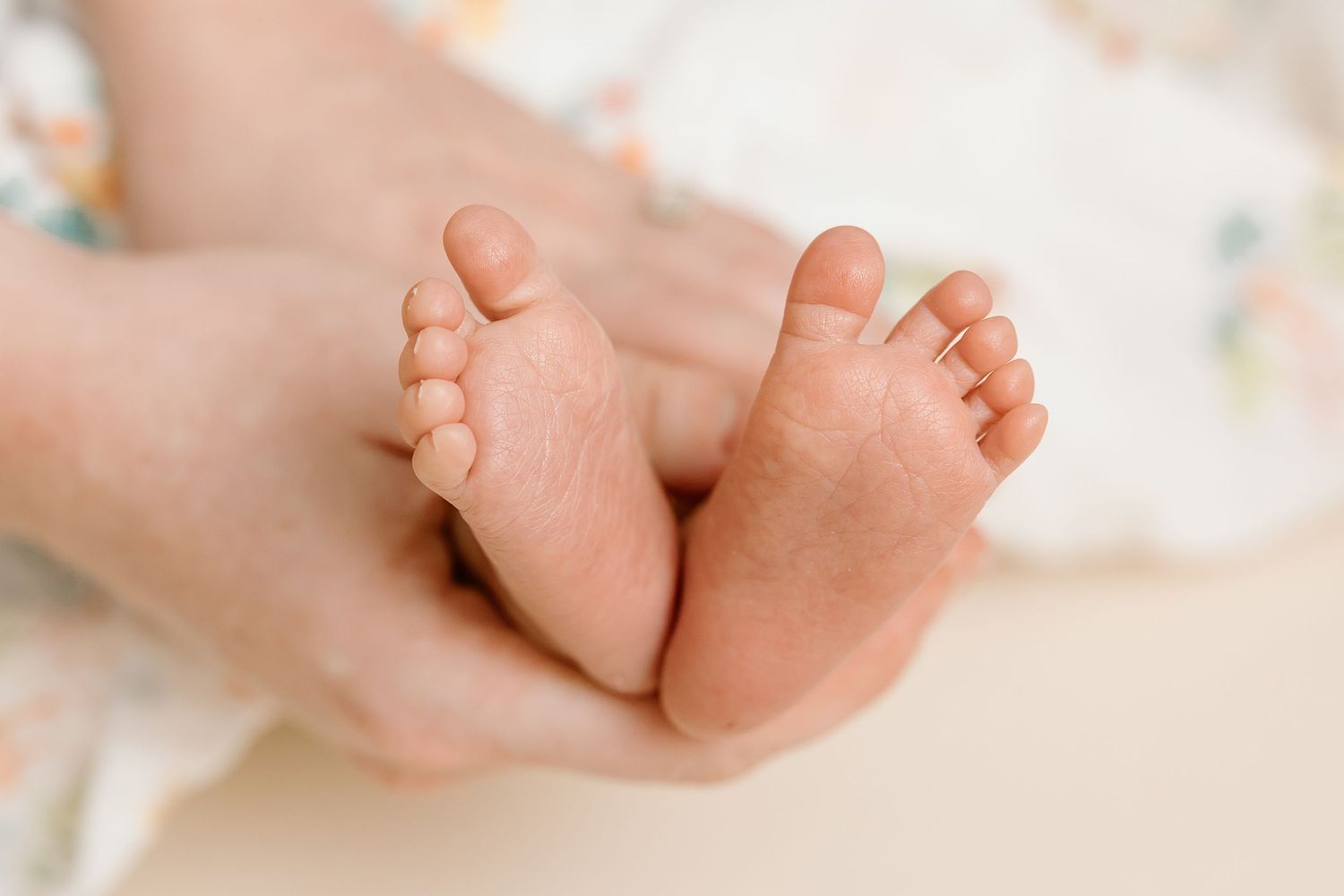 Tiny baby feet being gently held against light colored background.