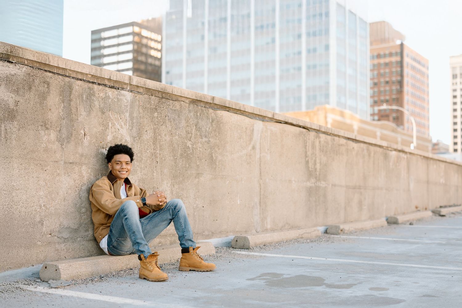 Urban lifestyle photo showing relaxed pose against concrete wall with city skyline.