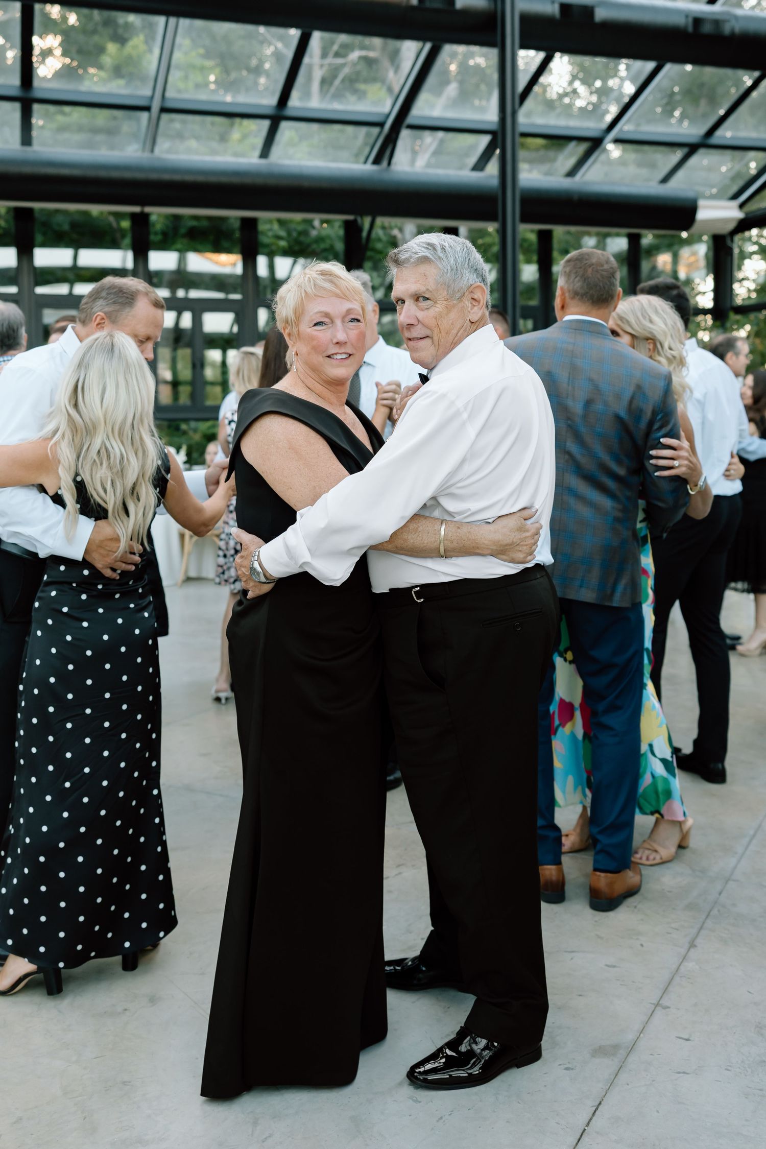 Elegant older couple dancing together at a formal wedding reception in a modern glass venue.