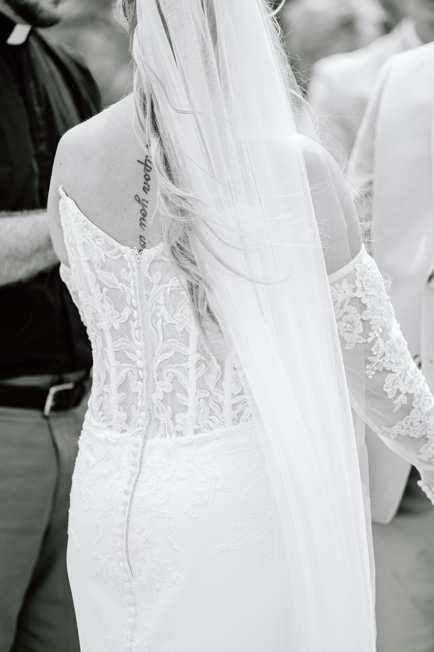 Black and white photo of bride in lace wedding dress with veil and shoulder tattoo.