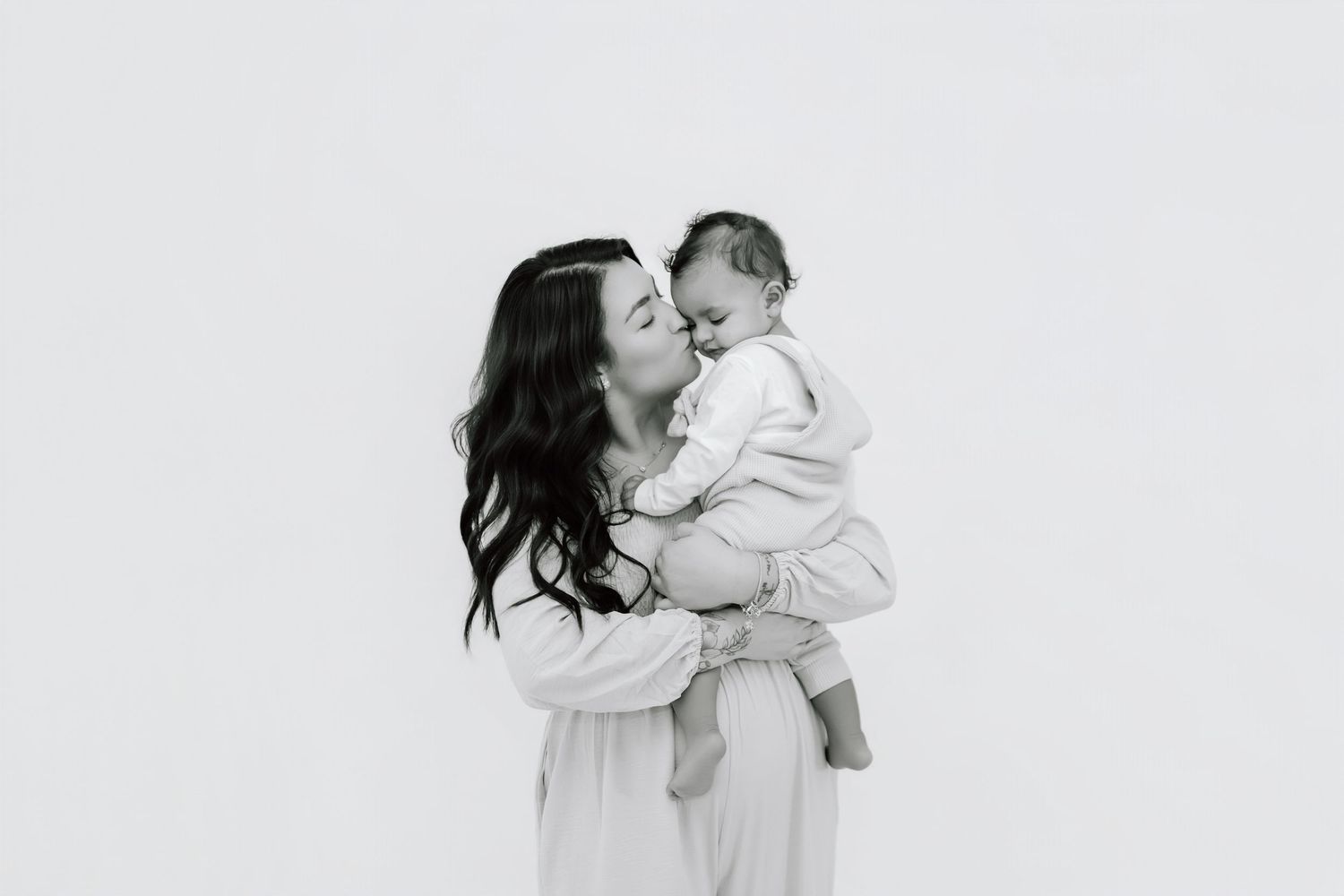 Black and white photo series showing tender moments between a parent and child against a light background.