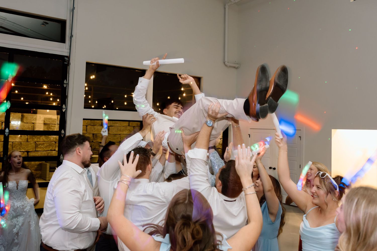 Joyful wedding celebration as guests lift the groom in the air during a lively reception dance party.