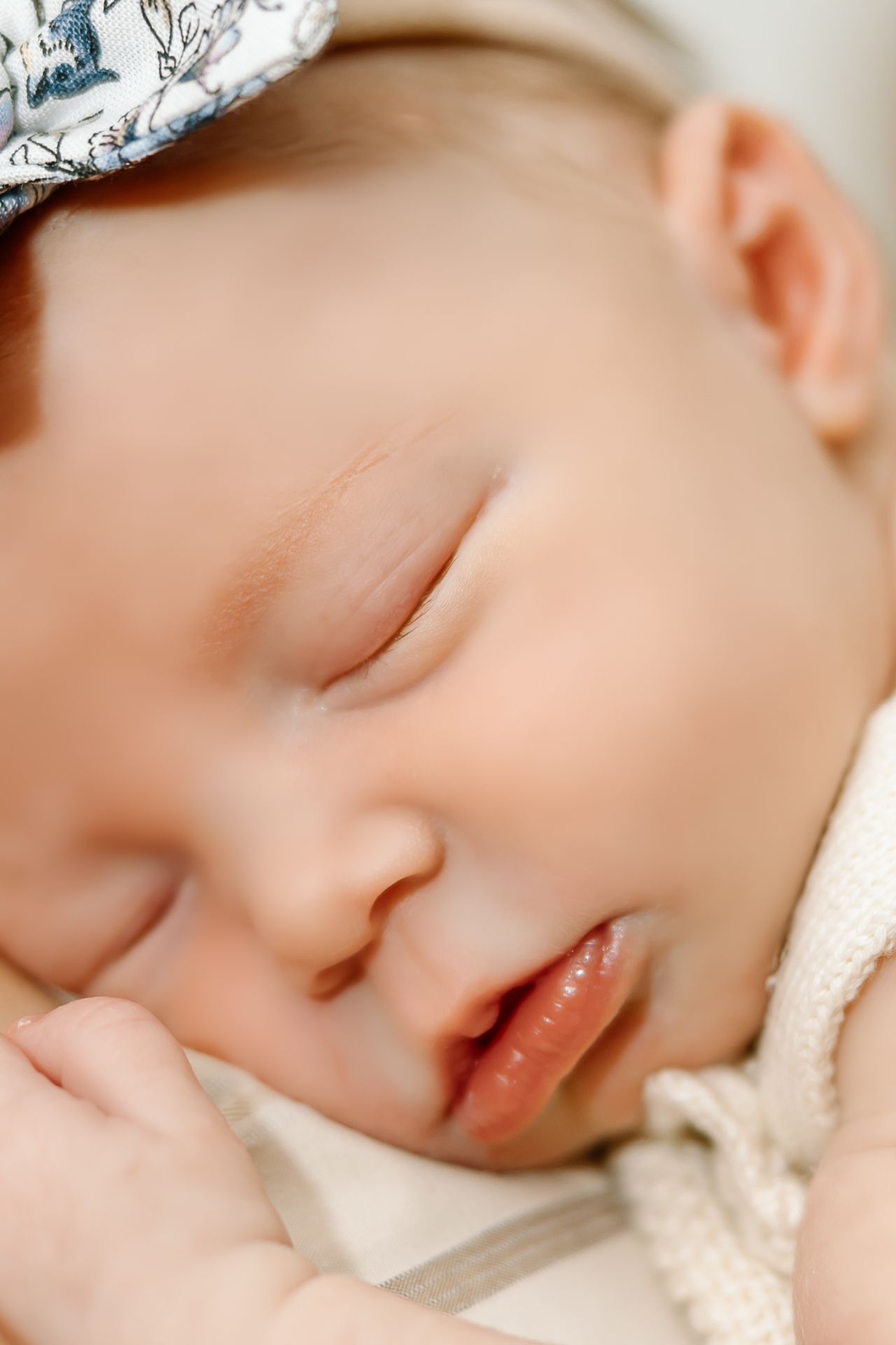 Close-up portrait of a sleeping baby wearing a delicate patterned headband.