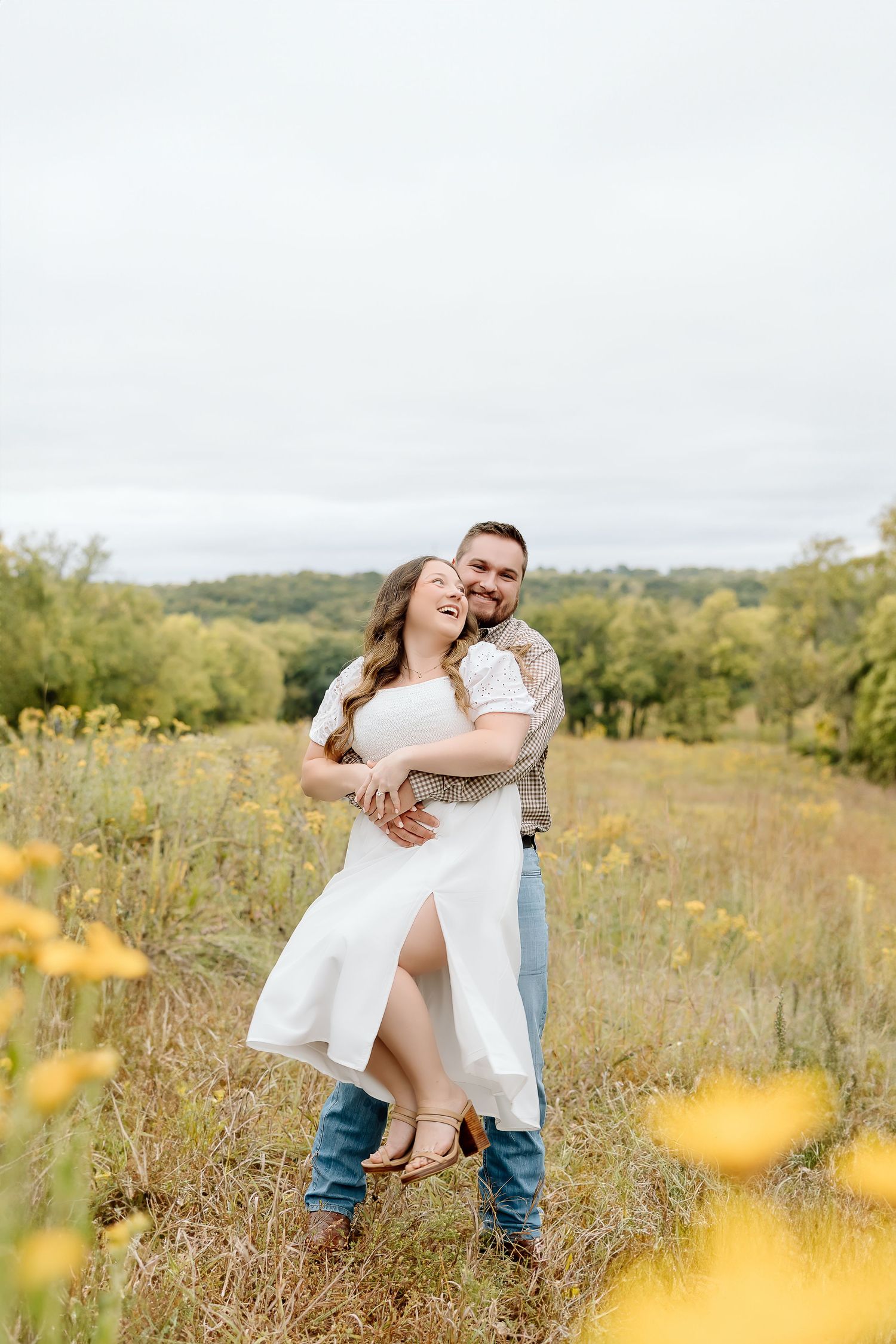 Joyful couple embracing and laughing in a sun-lit meadow with yellow wildflowers.