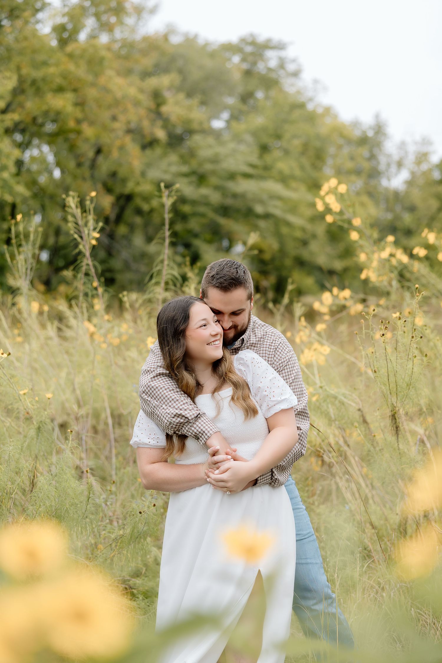 A romantic couple embraces in a field of yellow wildflowers at sunset.