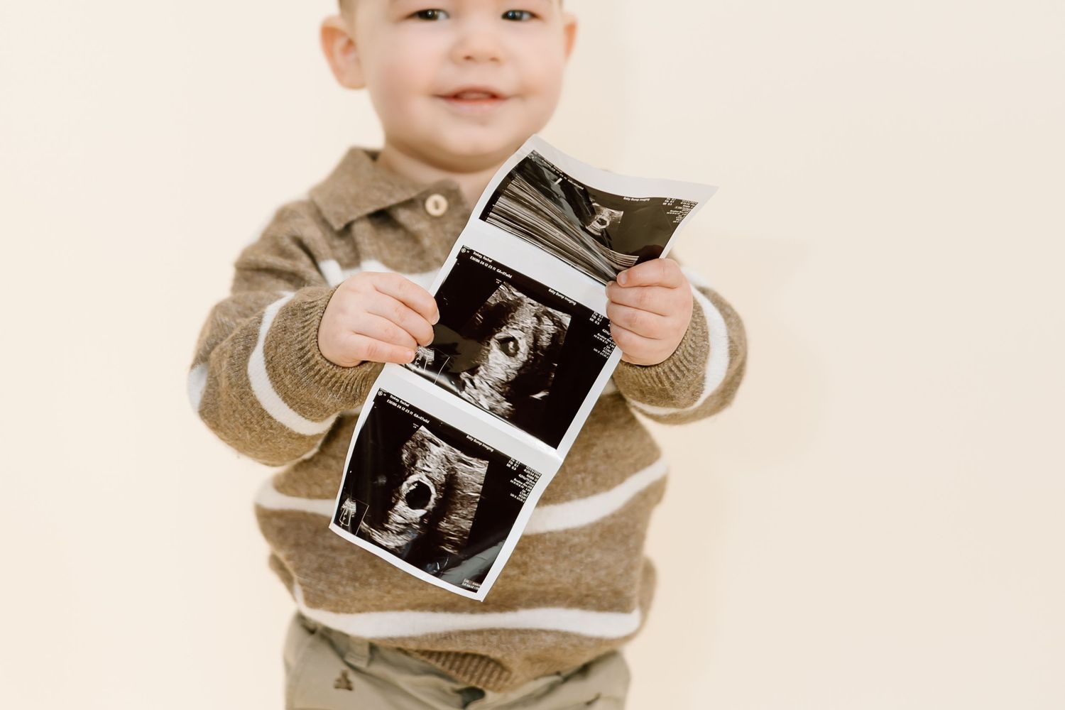 A small child wearing beige clothing holds and examines an ultrasound photograph.