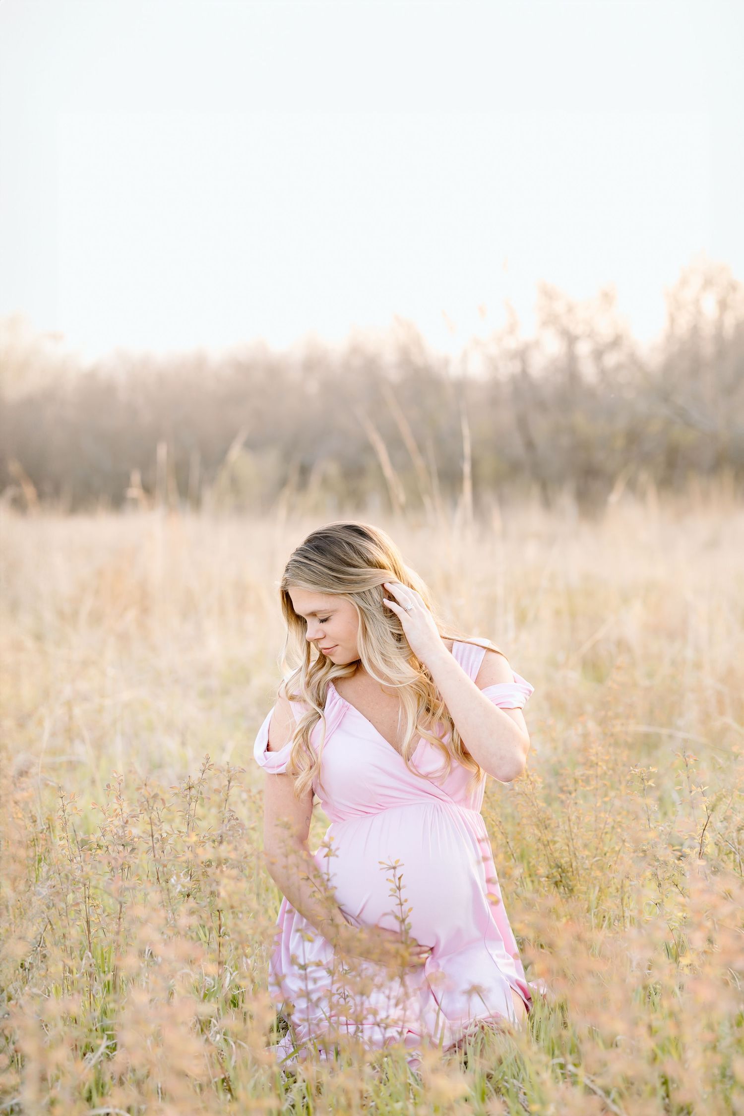 Person wearing pink dress sits in golden field of wildflowers at sunset creating dreamy outdoor portrait.