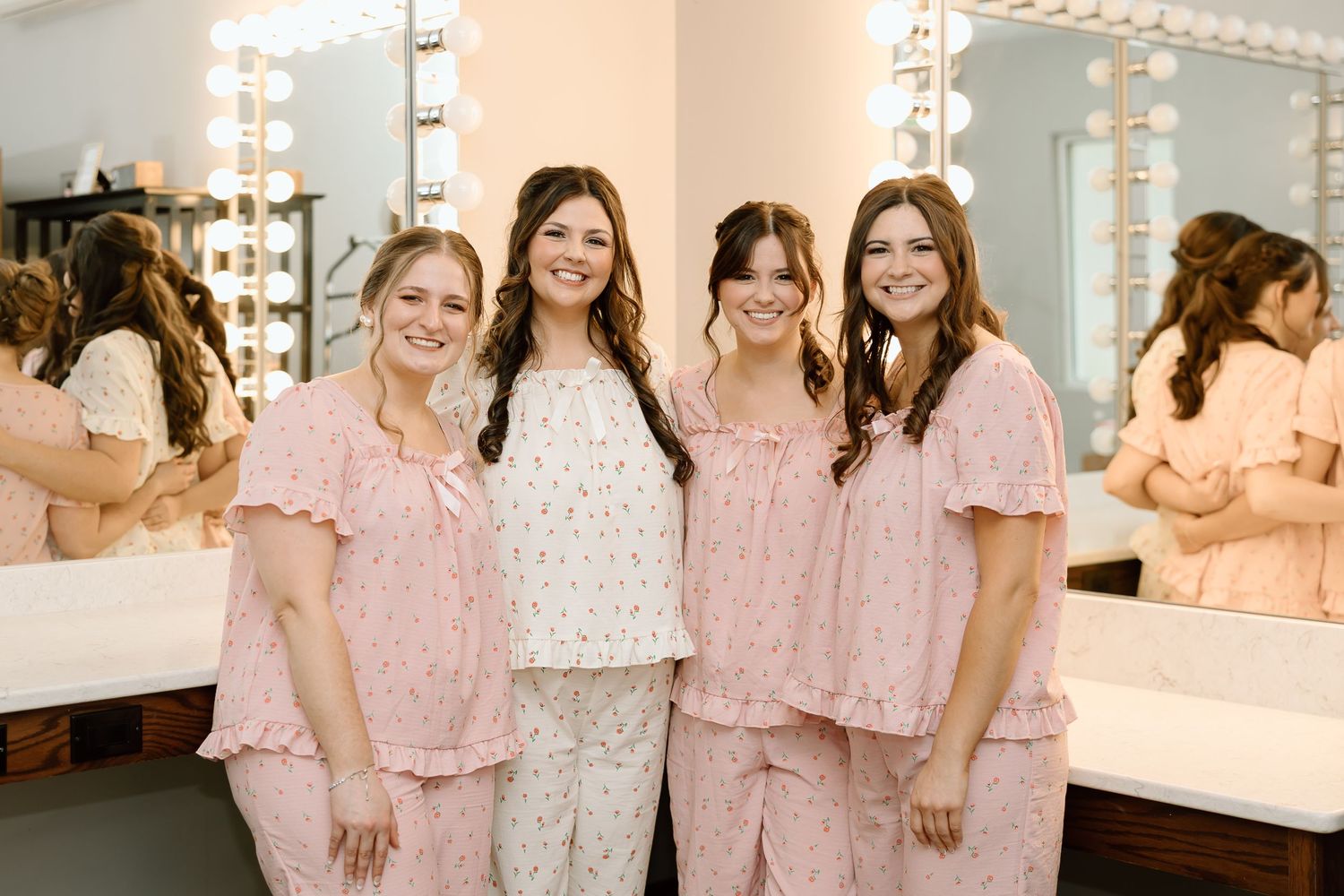 A group wearing matching pink floral robes poses together in a bridal suite getting ready for a wedding celebration.
