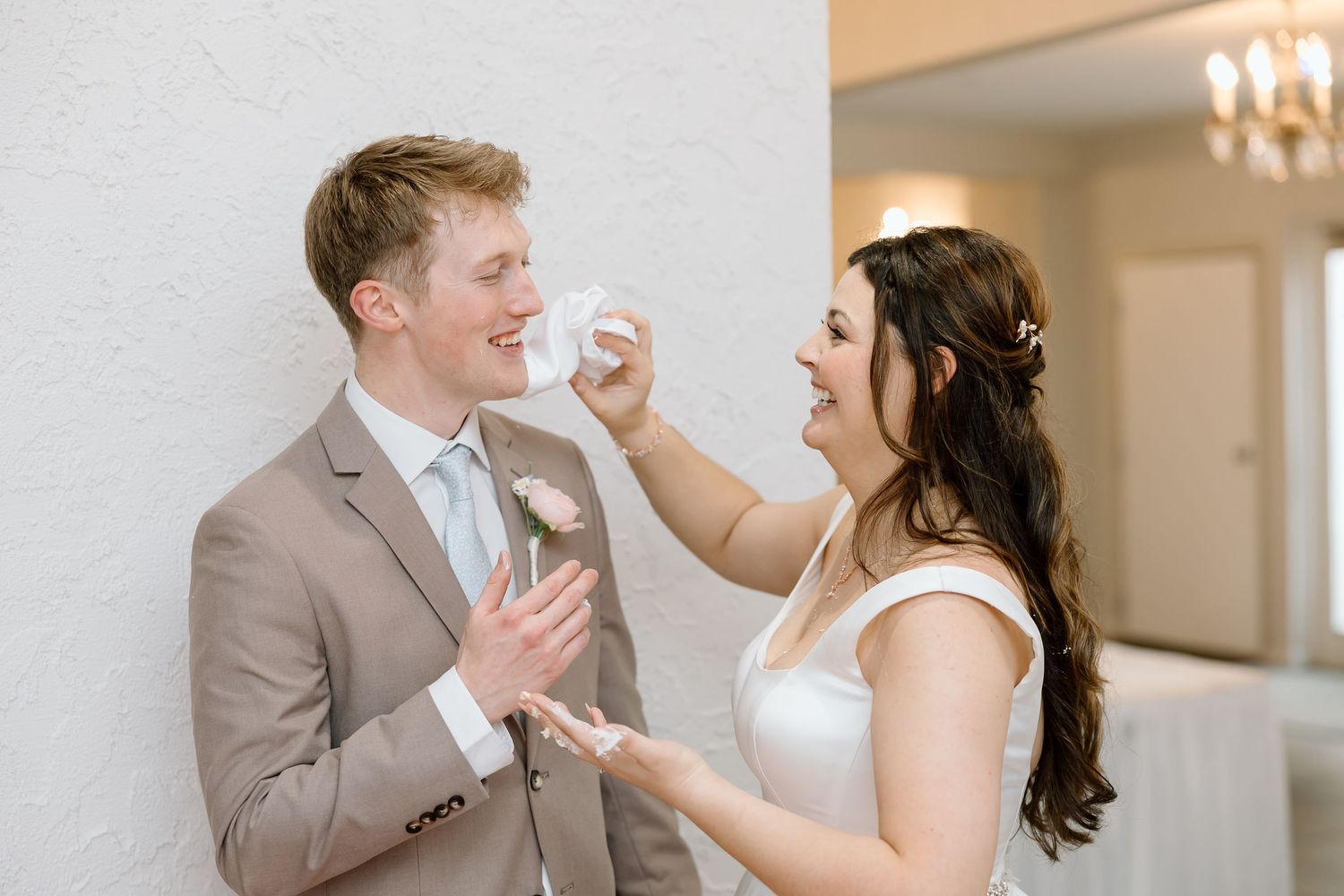 Bride and groom share a joyful moment dancing together in an elegant indoor venue with chandelier lighting.