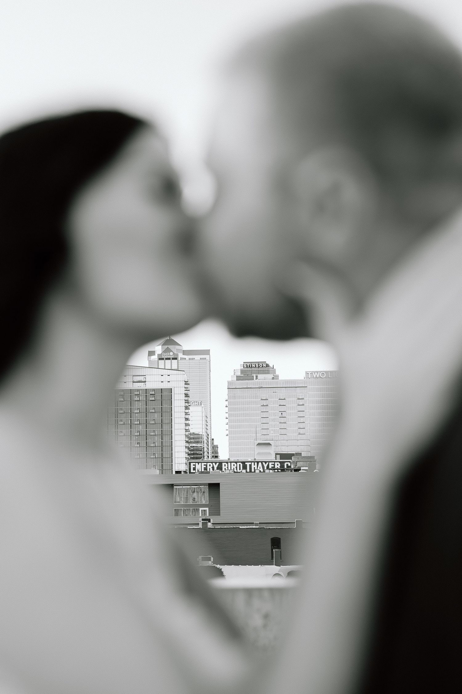 A black and white cityscape view framed through a heart-shaped opening, showing urban buildings and architecture.
