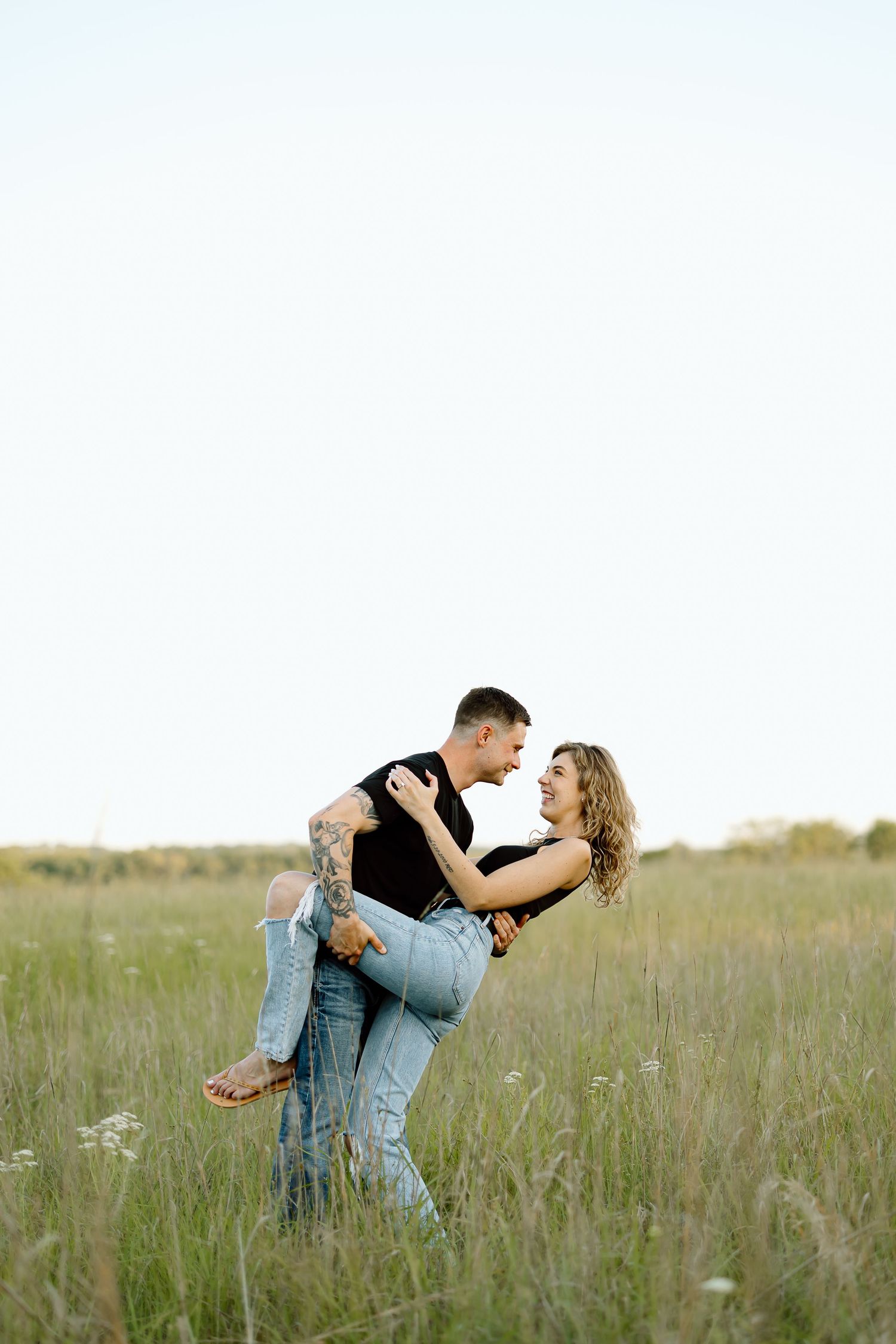 Romantic couple embracing in a tall grass meadow at sunset during a photo session.
