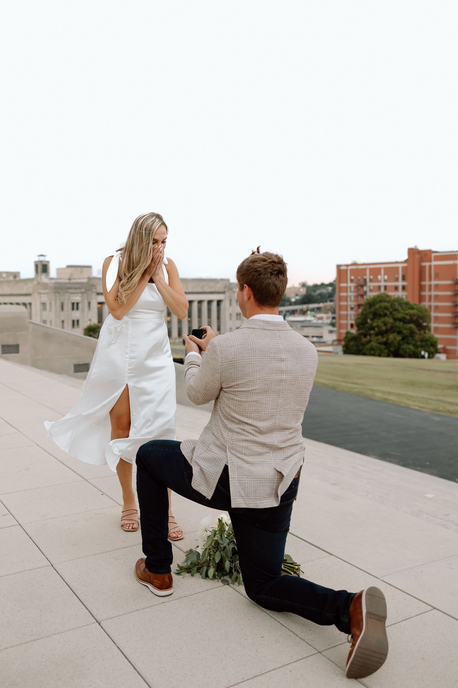 A couple gets engaged during a romantic rooftop proposal in an urban setting with a cityscape backdrop.