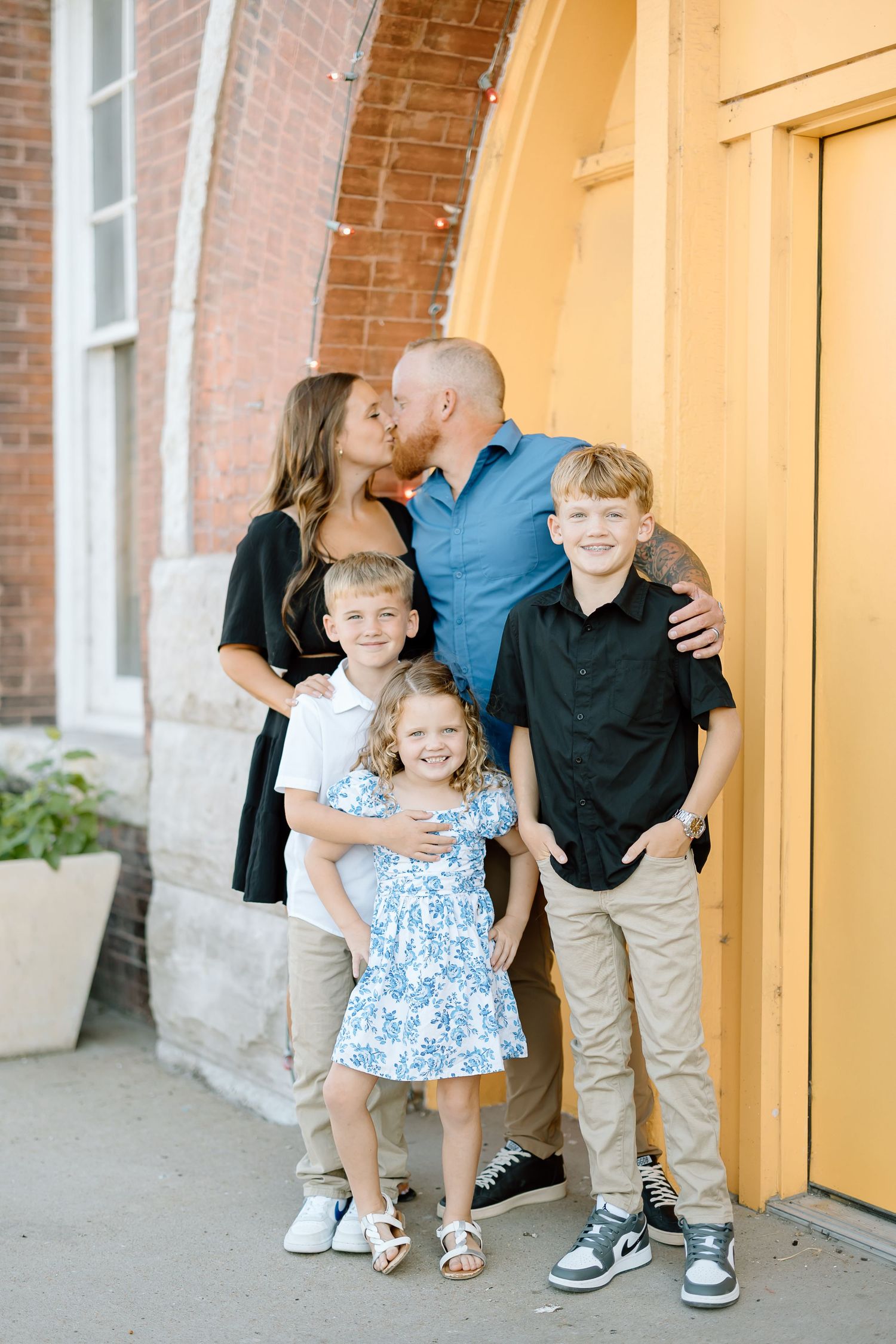 Three candid family portraits showing playful interactions in front of a brick building with orange columns.
