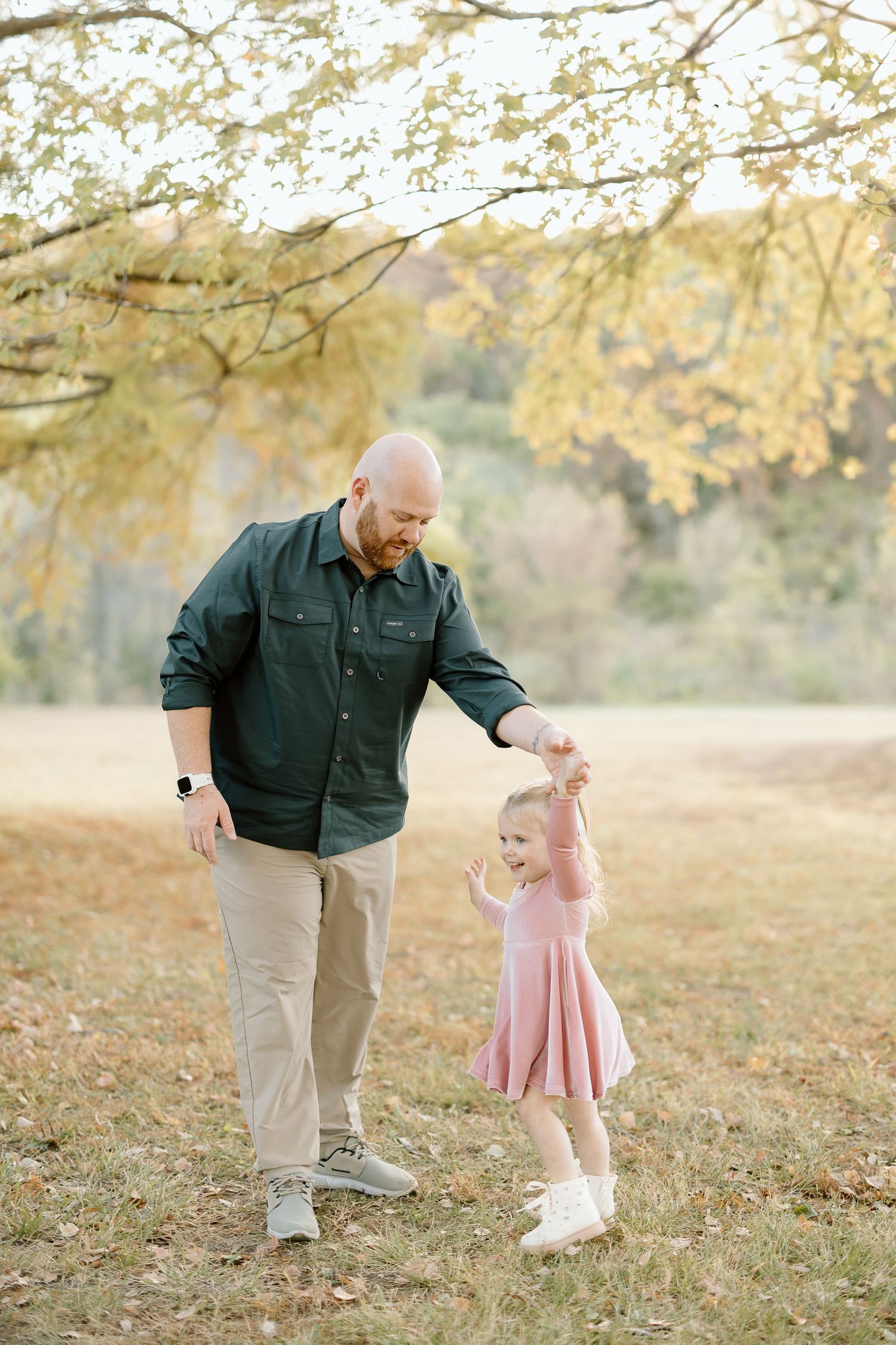 A sweet autumn scene shows a pair dancing and twirling together beneath golden leaves in a sunlit field.