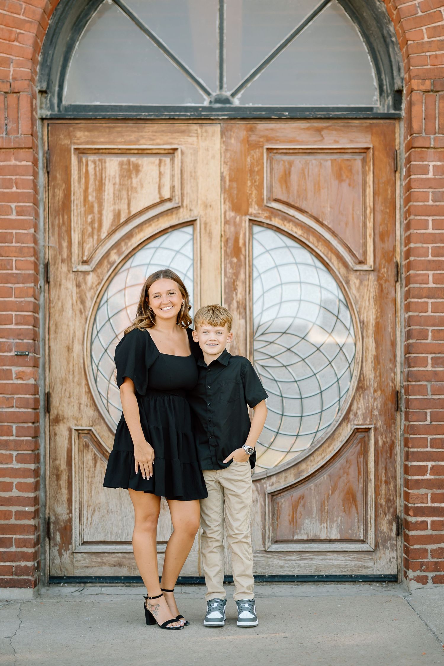 Family portrait session against rustic wooden doors and brick wall with decorative circular window details.