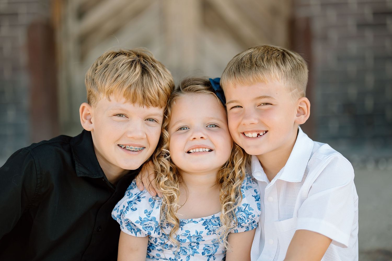 Three young children sit together and laugh while posing for a casual outdoor portrait session.