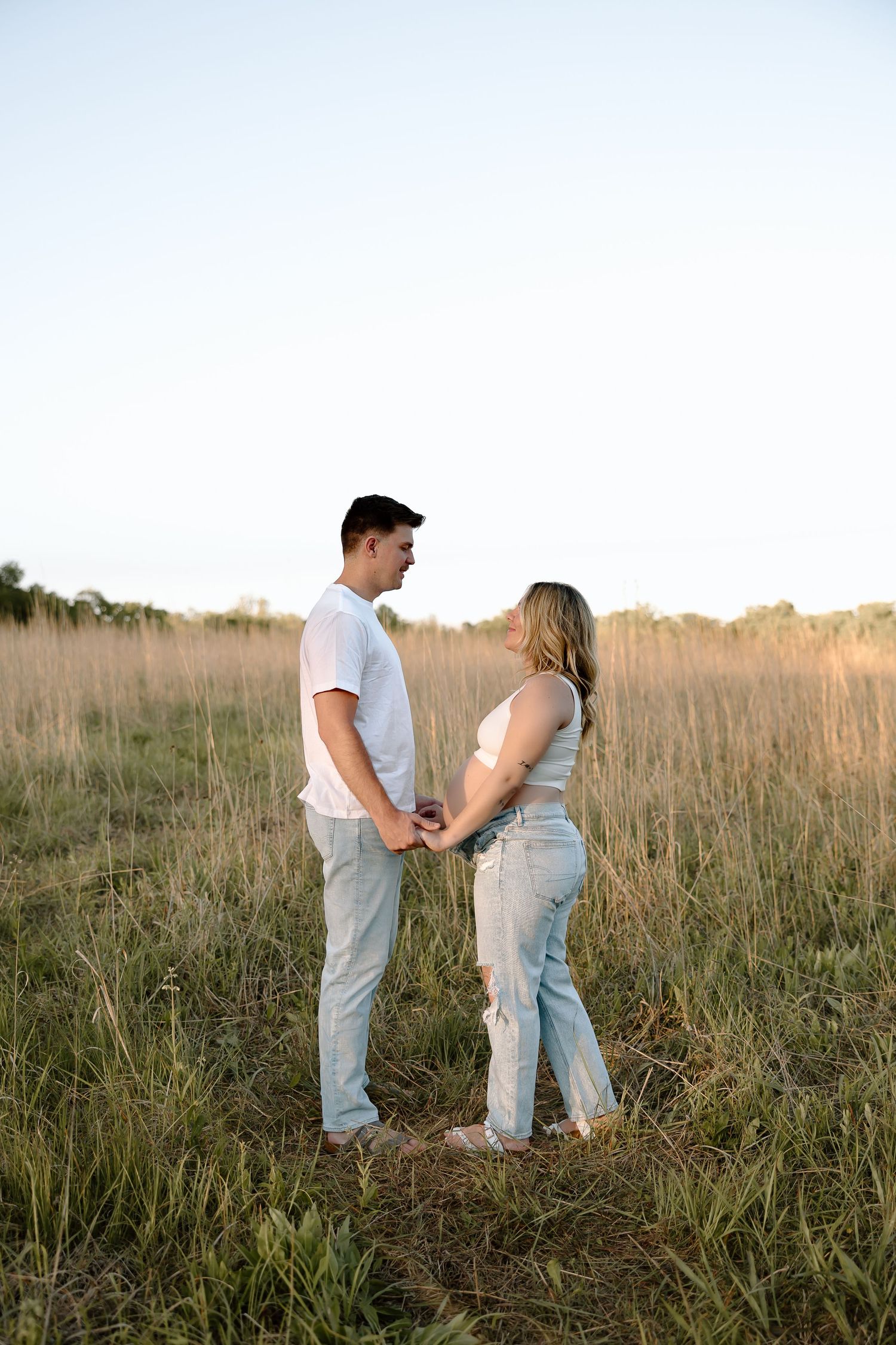 A couple shares a tender moment together in a golden sunlit field of tall grass at sunset.