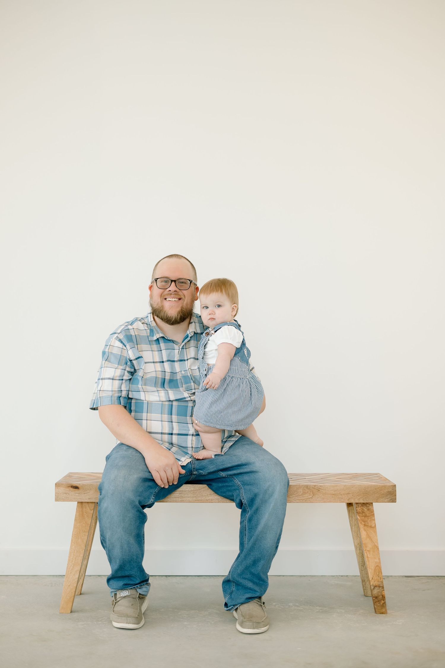A person sits with a small child on a wooden bench against a white wall in a series of minimalist photos.
