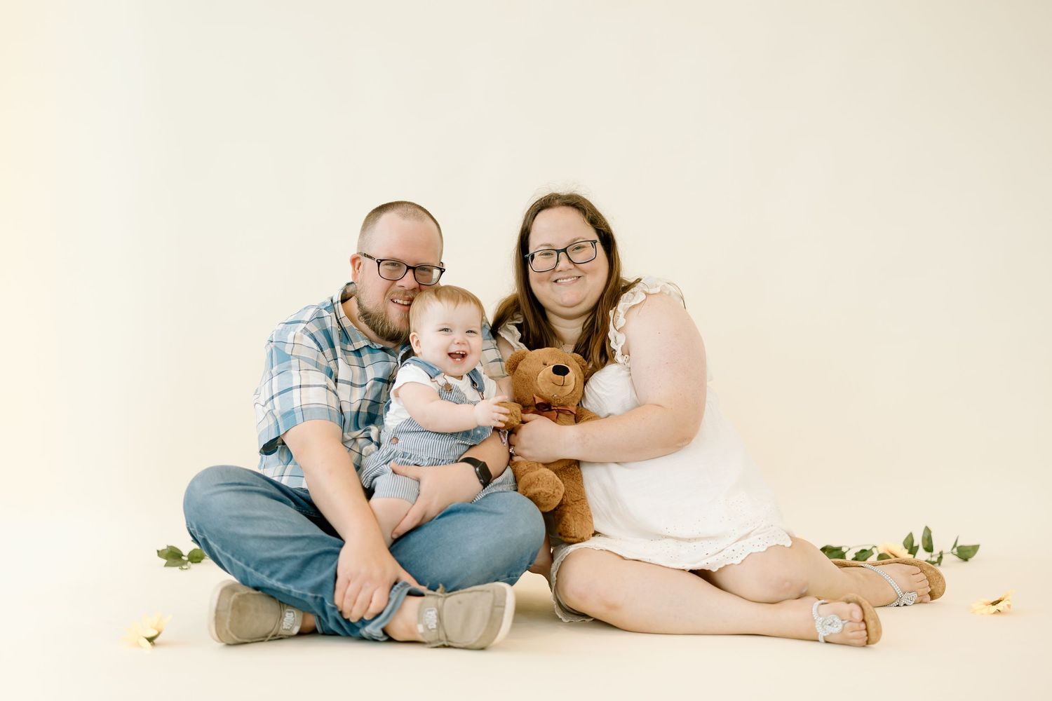 A family in coordinating denim outfits relaxes together on a light beige backdrop for a casual portrait session.