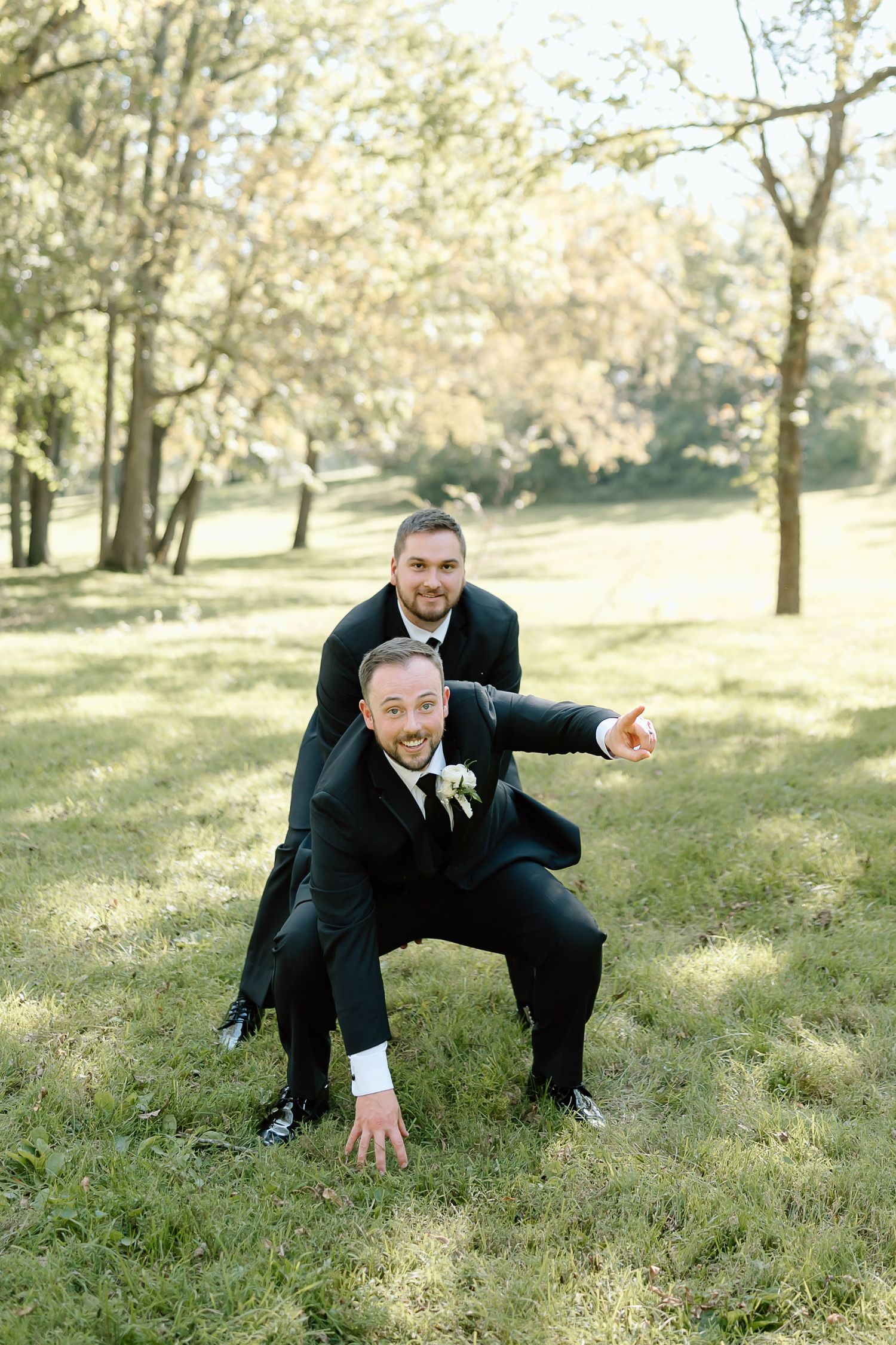 Playful sequence of someone in a black suit crouching and pointing in a sunlit grassy park setting.