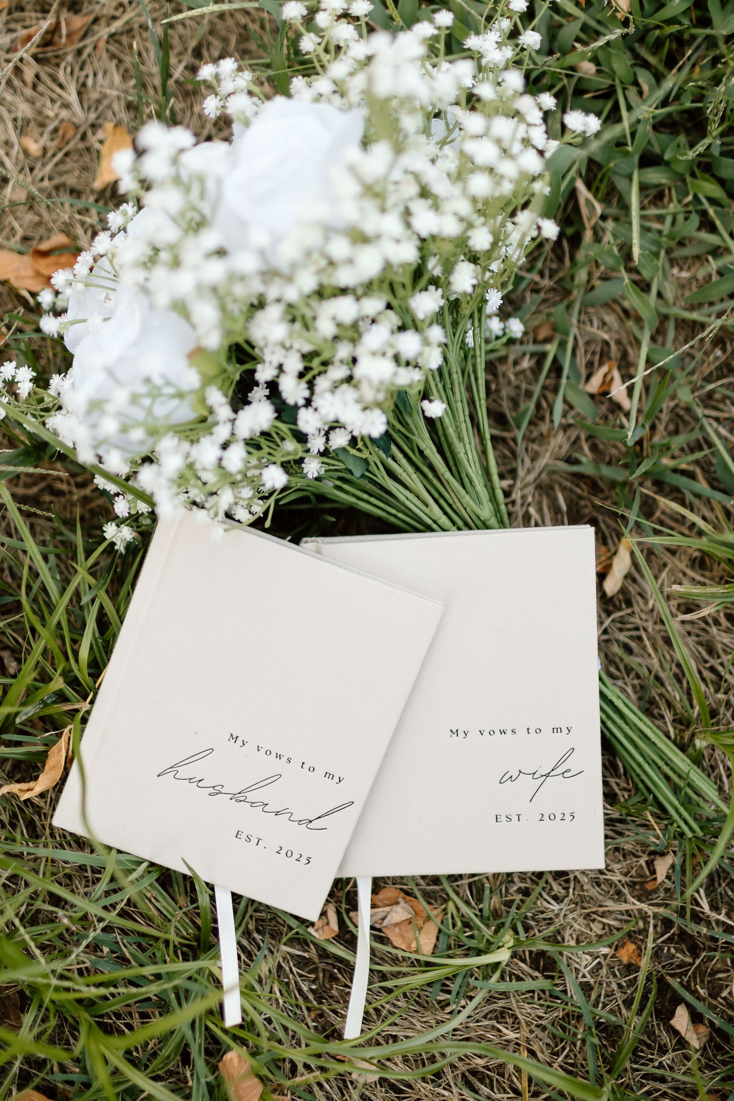Small white place cards with elegant handwriting text scattered on grass and white flowers in an outdoor setting.