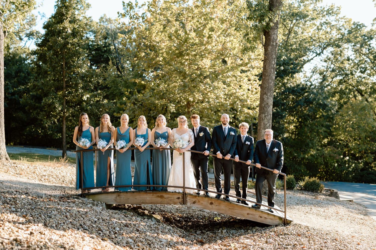 A wedding party stands in a line on a hillside path during an outdoor autumn ceremony.