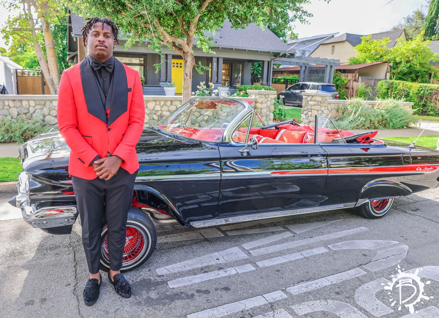 A red and black lowrider car is displayed in front of a residential home during daytime. Prom Party.