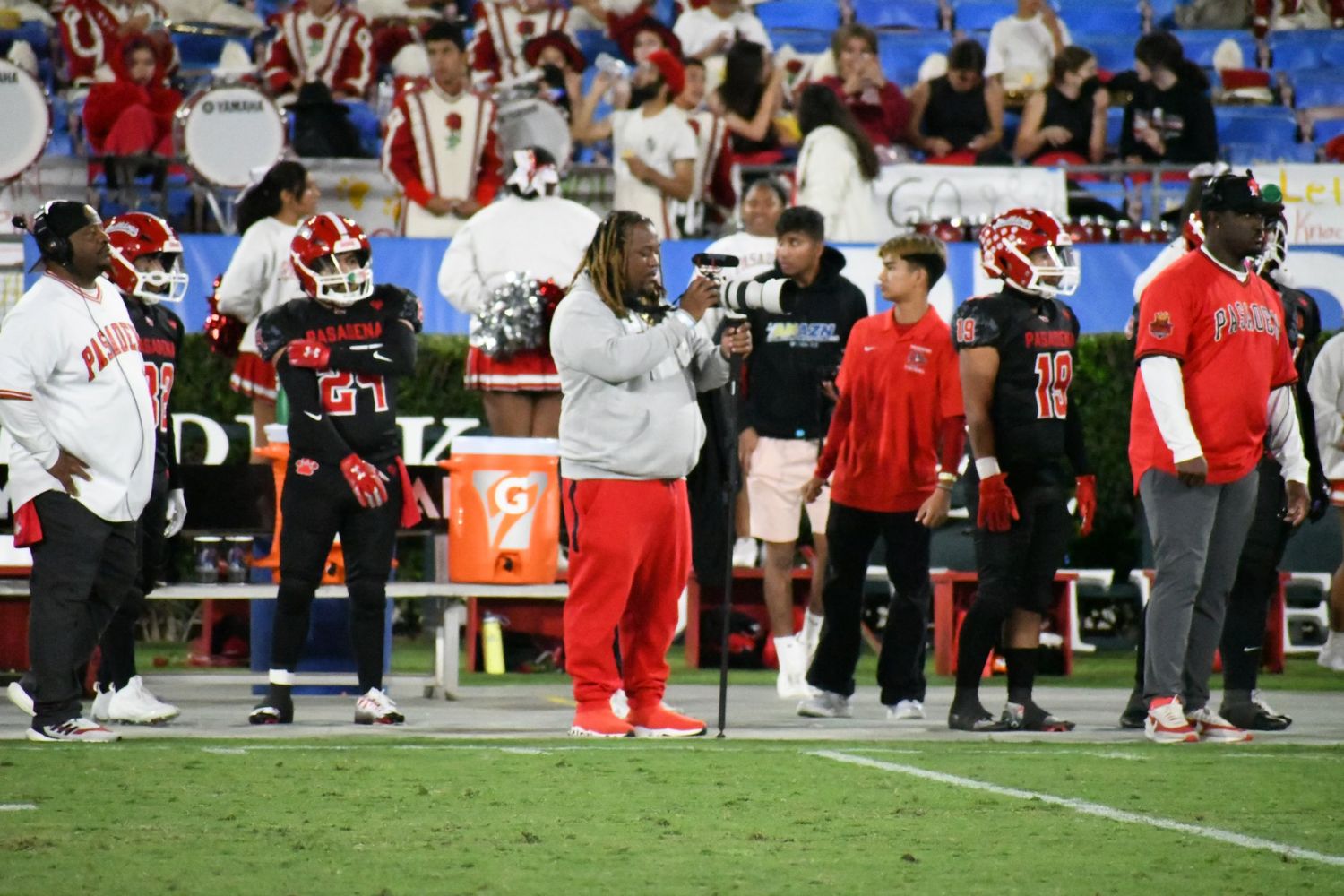 Football players and coaches gather on the field during a game against red and white uniformed teams.
