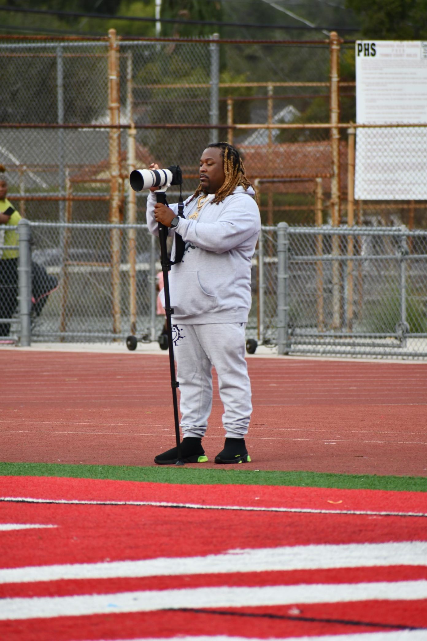 A photographer kneels on a red running track taking photos with a professional camera and long lens.