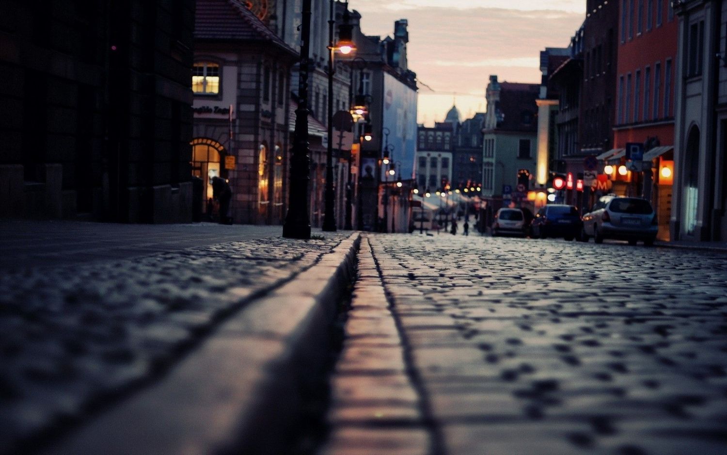 Long shadows stretch across illuminated cobblestone streets during a quiet evening in an urban setting.